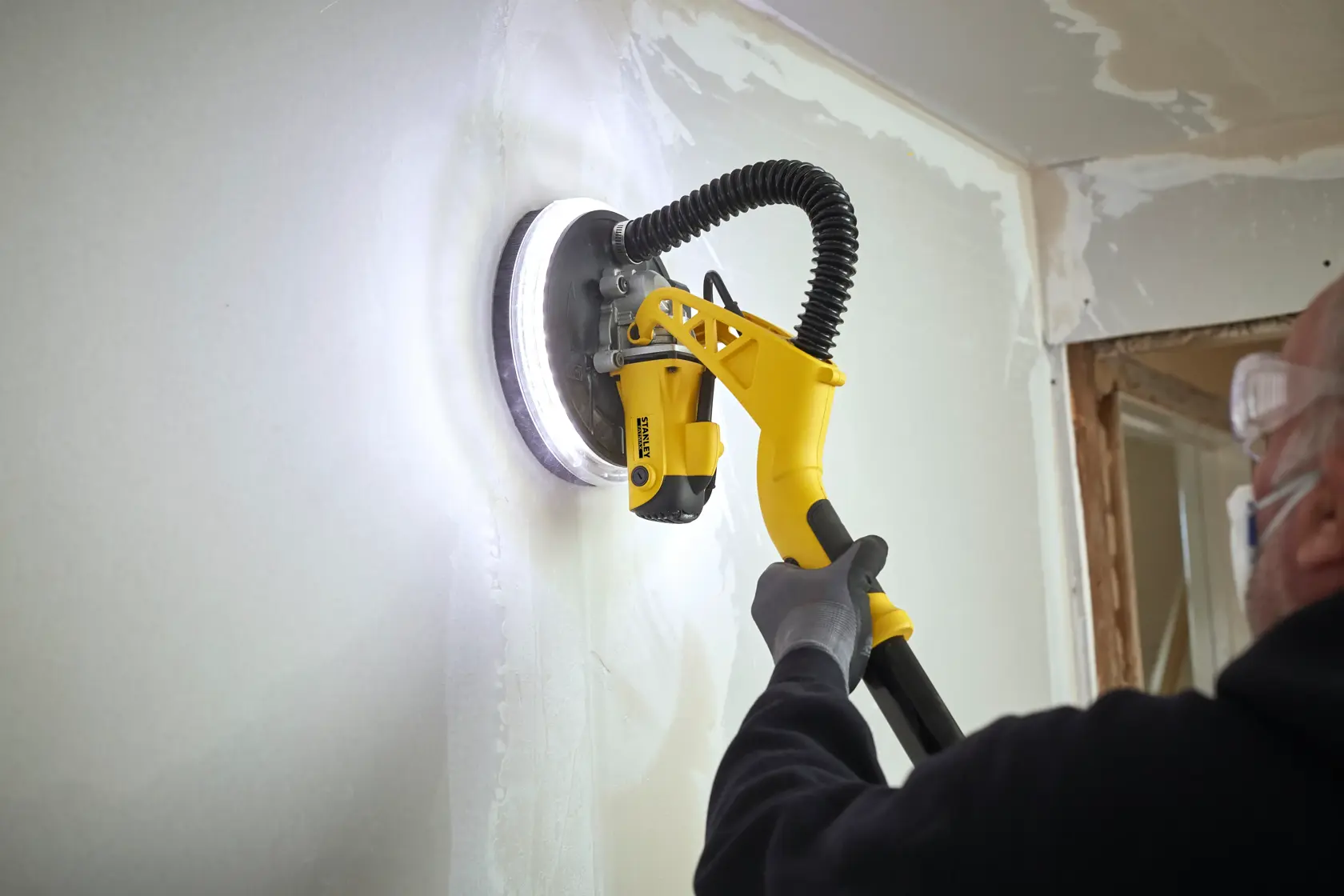 STANLEY SFMEE500S levigatrice per cartongesso in uso, manico giallo, levigando parete bianca, primo piano.