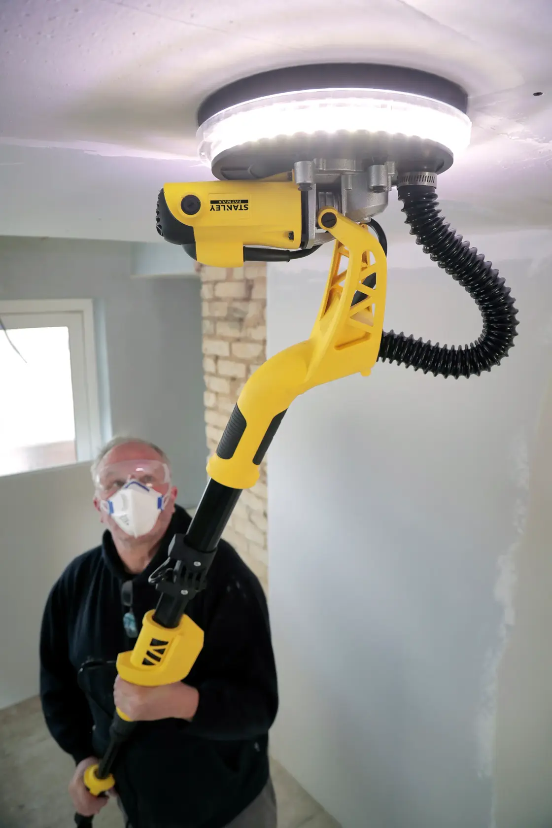 Levigatrice per cartongesso STANLEY SFMEE500S in uso, utensile giallo e nero con luce LED, levigando un soffitto.