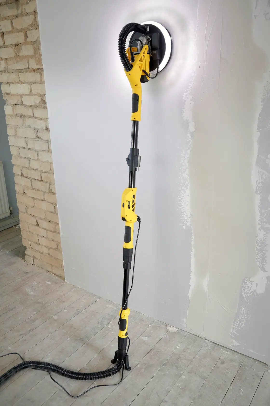 Levigatrice per pareti STANLEY SFMEE500S con luce LED, manico telescopico, levigando parete in gesso, vista laterale.