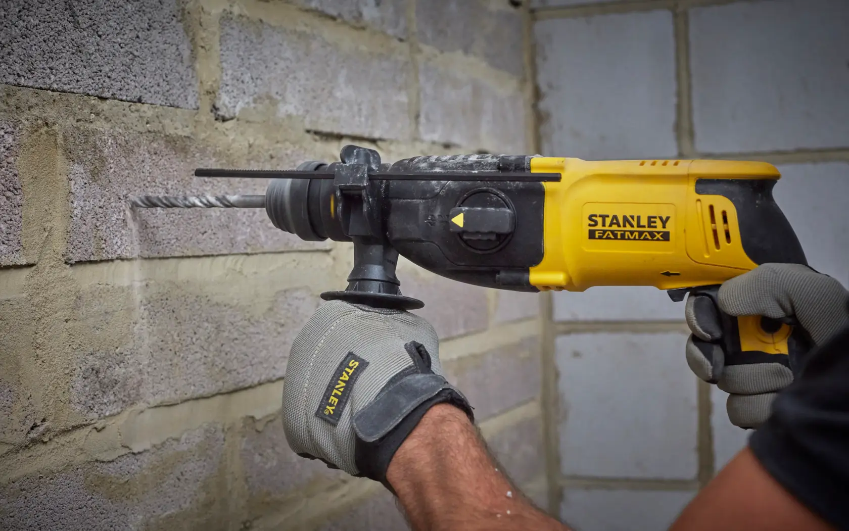 Foto del martello rotativo STANLEY SFMEH210K-QS in uso su un muro di mattoni, design giallo e nero.