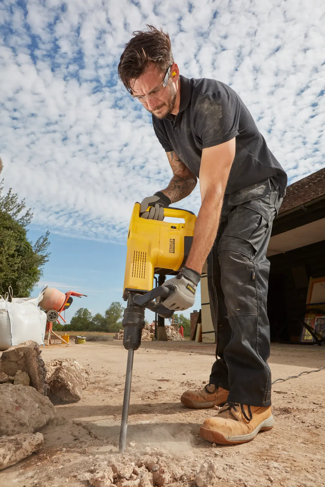 Foto di una persona che utilizza il martello demolitore STANLEY SFMEH230K-QS su cemento esterno, scena di cantiere.