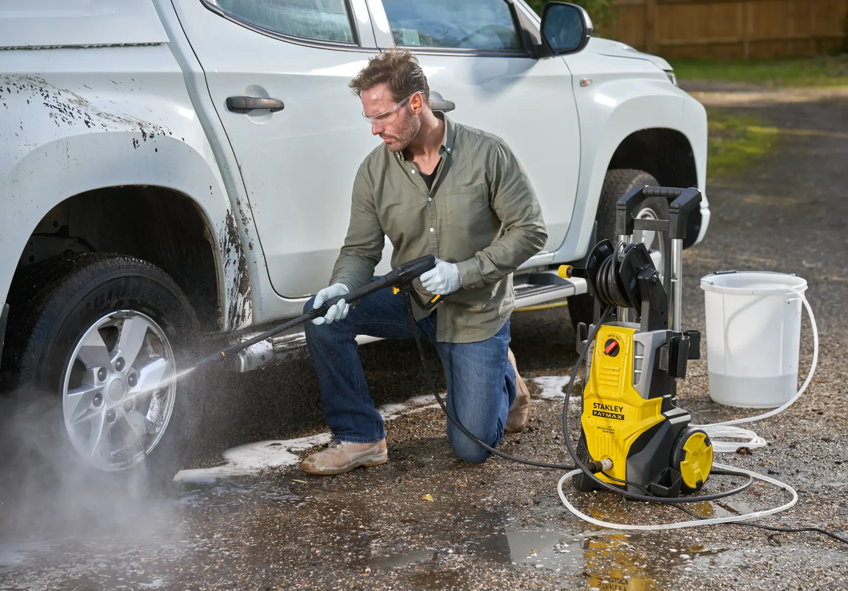 Stanley SFMPW2400 idropulitrice pulisce ruota auto all'aperto; unità gialla, tubo, secchio visibili.