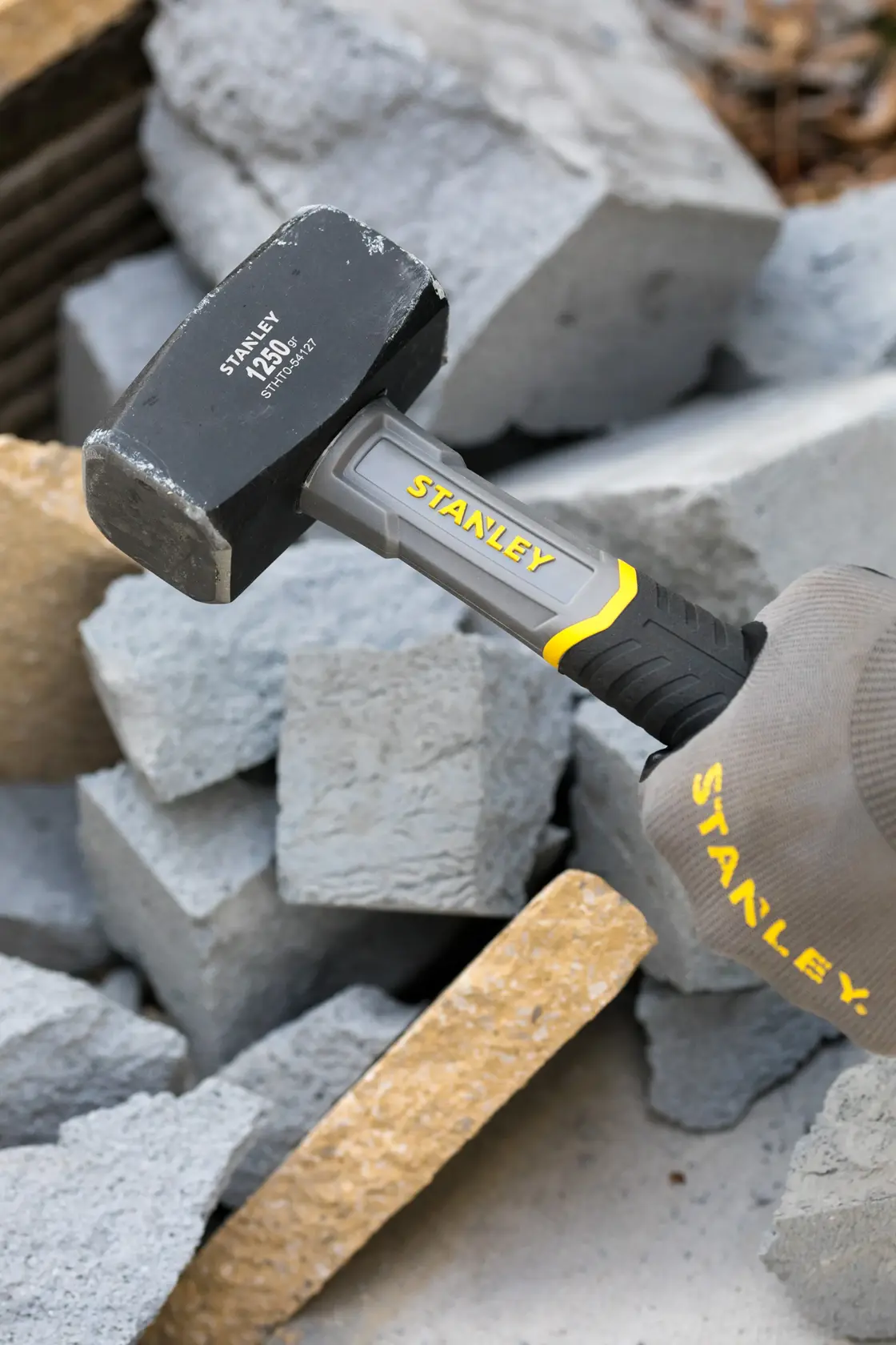 Foto del mazzuolo STANLEY STHT0-54127 con manico grigio e giallo che rompe blocchi di cemento.