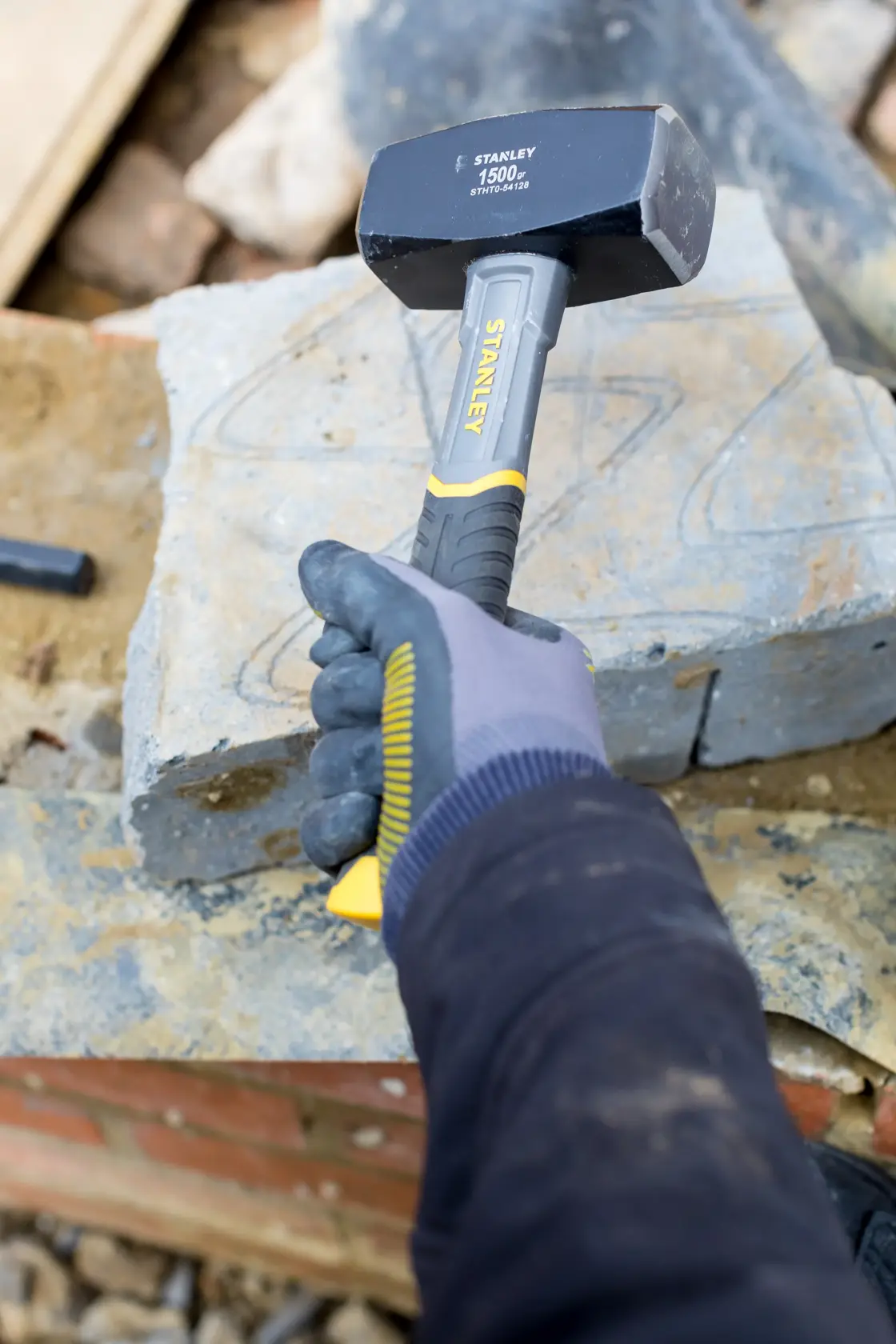 Martello STANLEY STHT0-54128 con manico giallo e nero tenuto da mano guantata su cantiere in pietra.