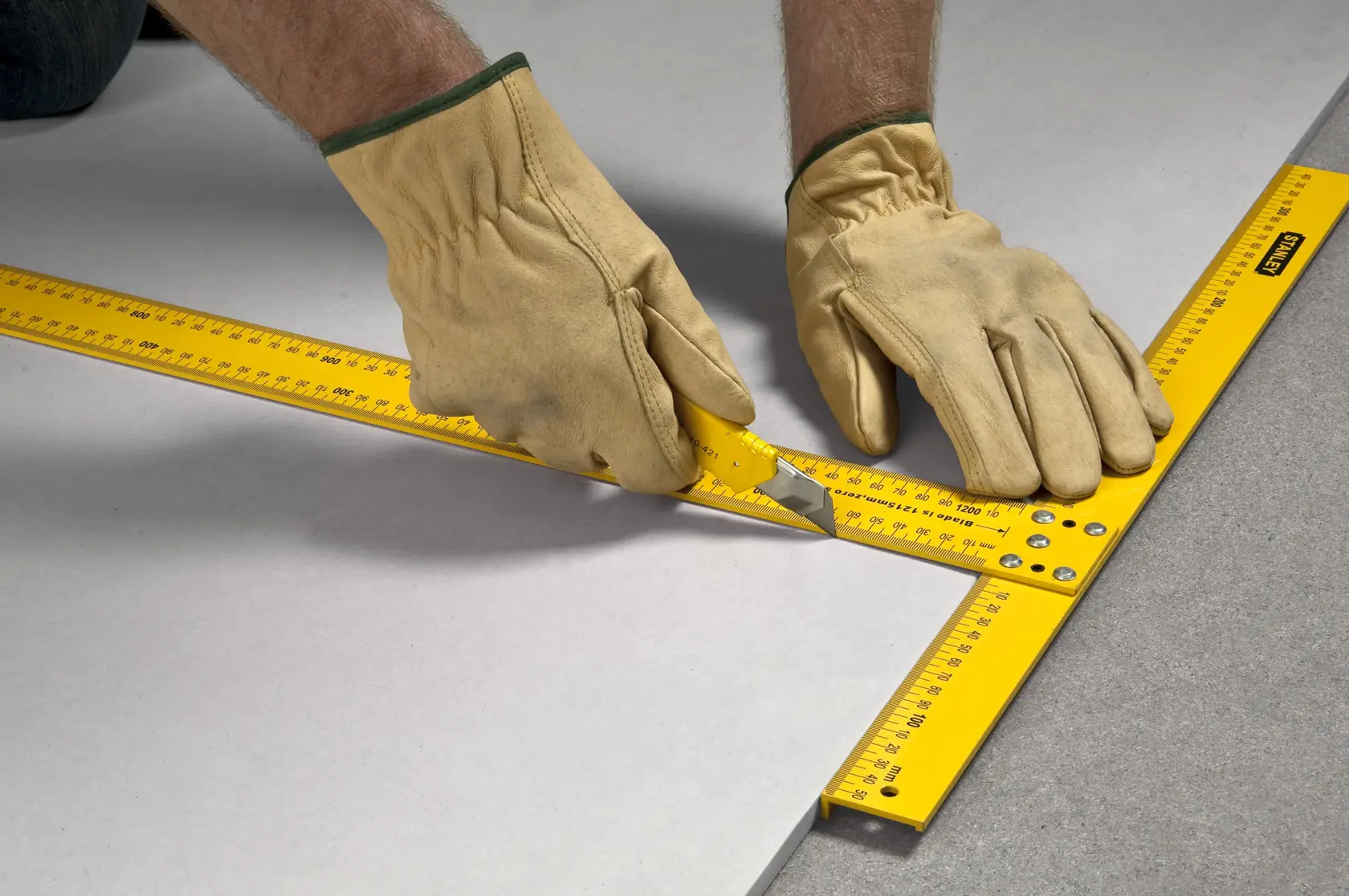 STANLEY STHT1-05894 squadra gialla per cartongesso usata da mani con guanti su superficie piana.