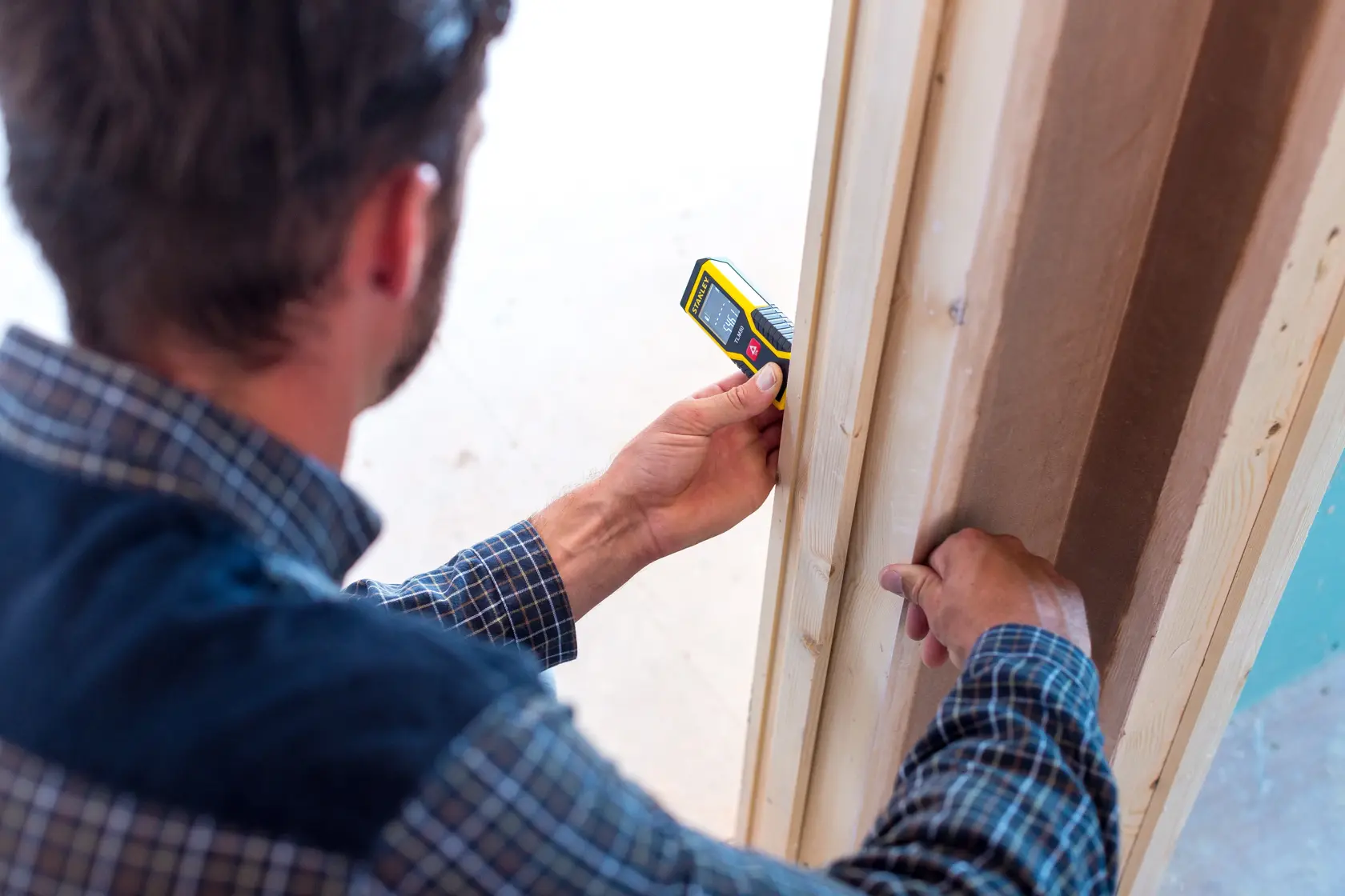 Stanley STHT1-77409 misuratore di distanza laser digitale usato da una persona per misurare un telaio di porta in legno.