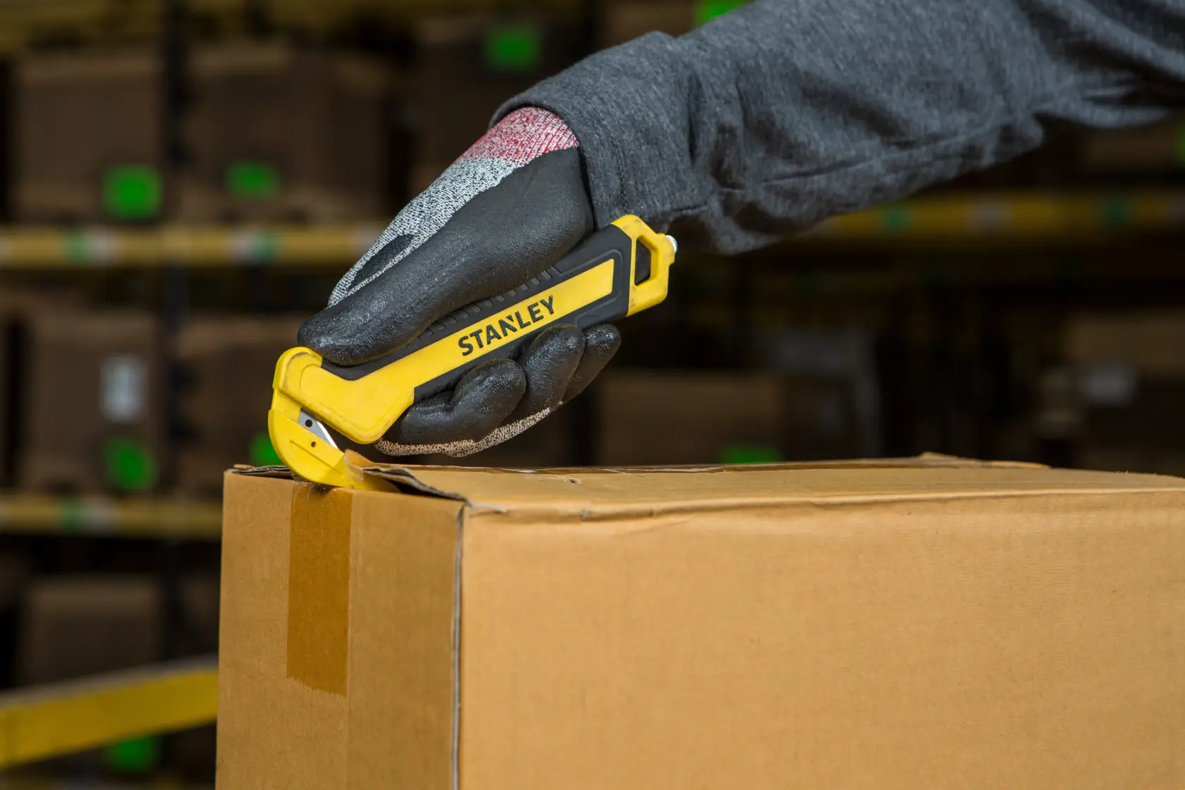 STANLEY STHT10356-0 coltello di sicurezza taglia scatola di cartone, tenuto in mano, sfondo magazzino.