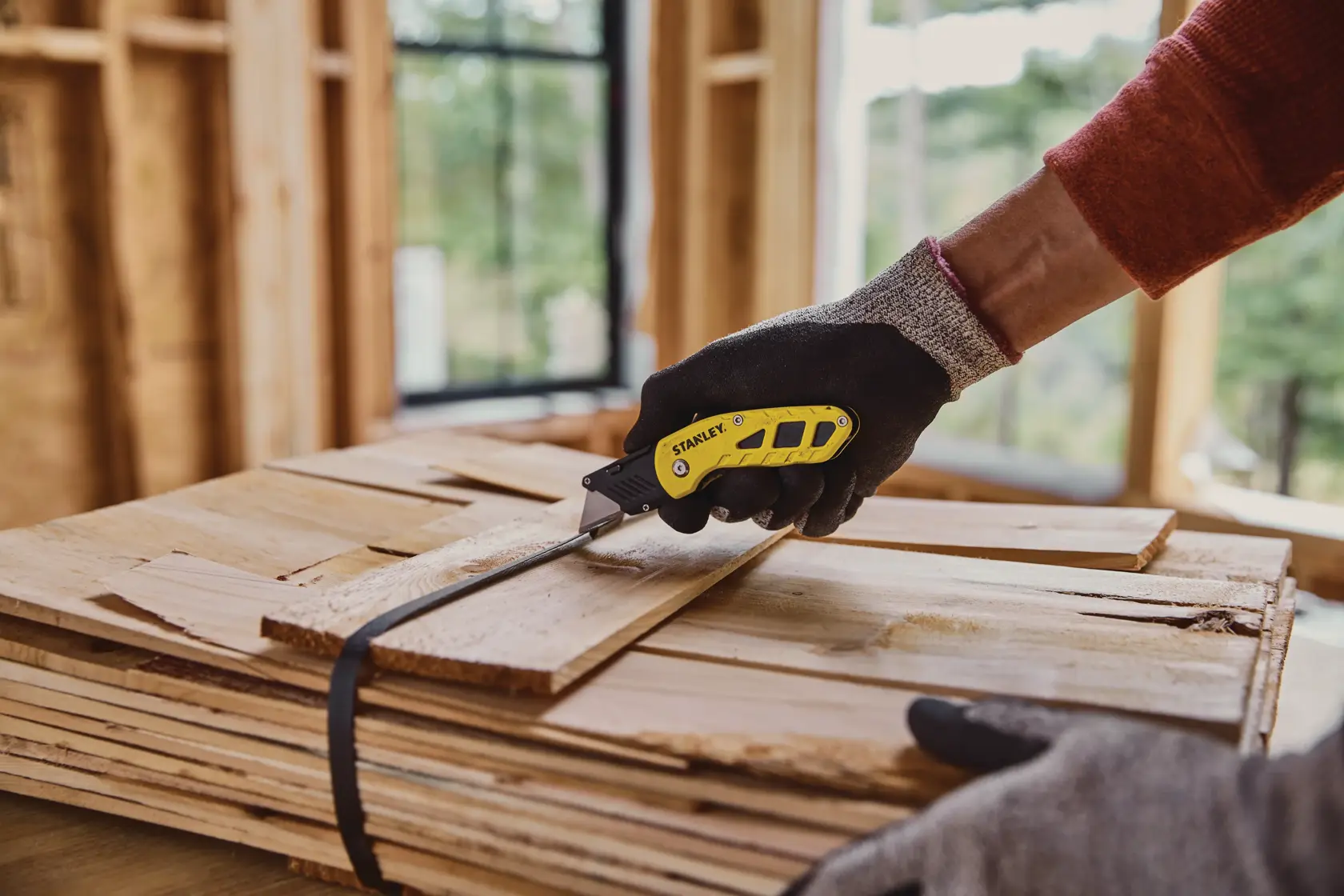 Fotografia del coltello universale pieghevole STANLEY STHT10424-0 che taglia una cinghia di legno in cantiere.