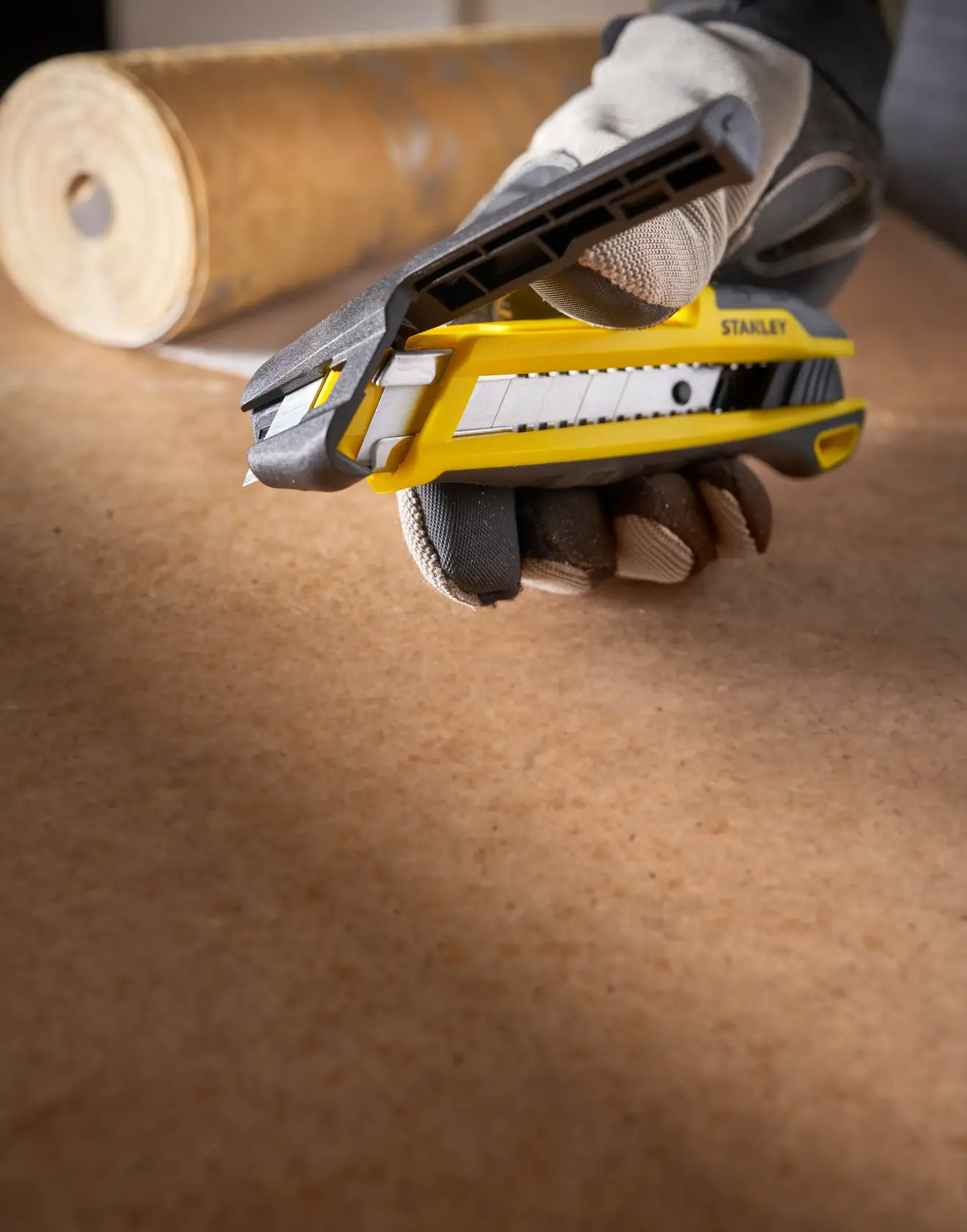 STANLEY STHT10501-0 taglierino giallo e nero tenuto da una mano guantata su piano di lavoro, angolo laterale.