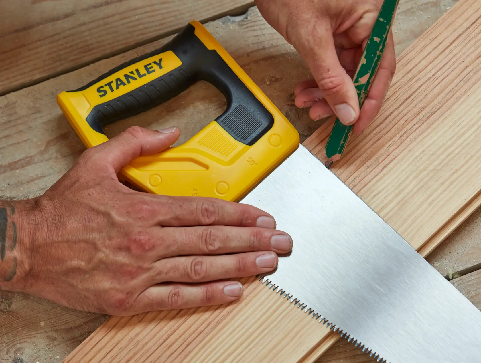 Stanley STHT20350-1 seghetto manuale con manico giallo e nero su legno, persona segna con matita.