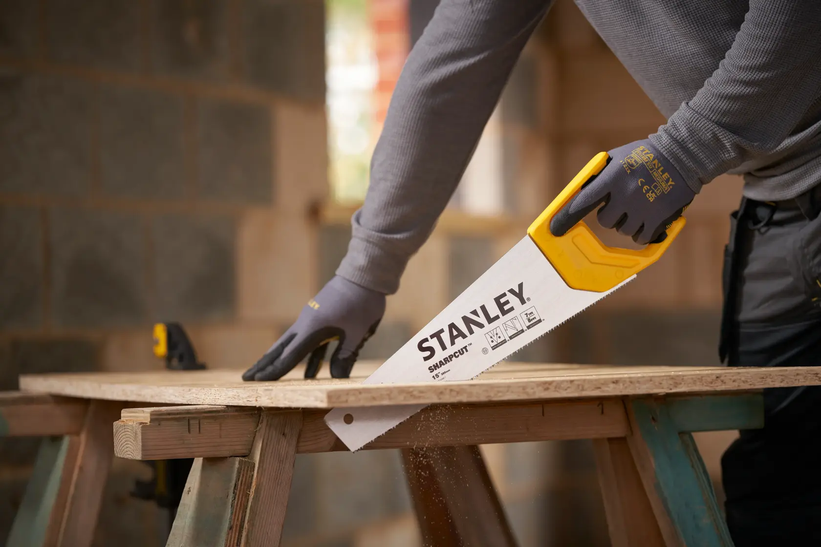 Foto del seghetto manuale STANLEY STHT20366-1 con manico giallo mentre taglia legno, usato da persona con guanti.