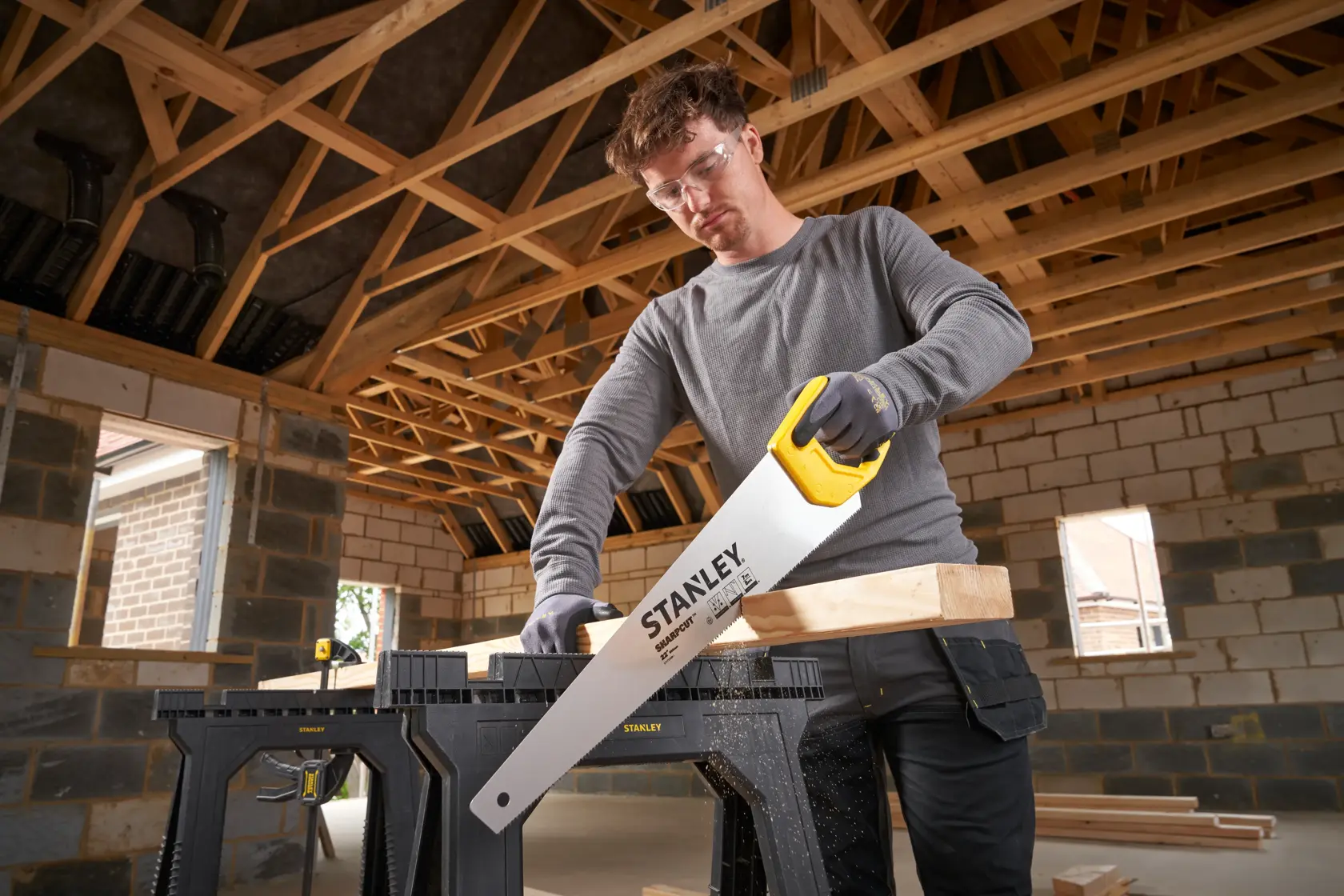 Foto del segaccio STANLEY STHT20368-1 con manico giallo che taglia legno su cavalletto nero in cantiere.