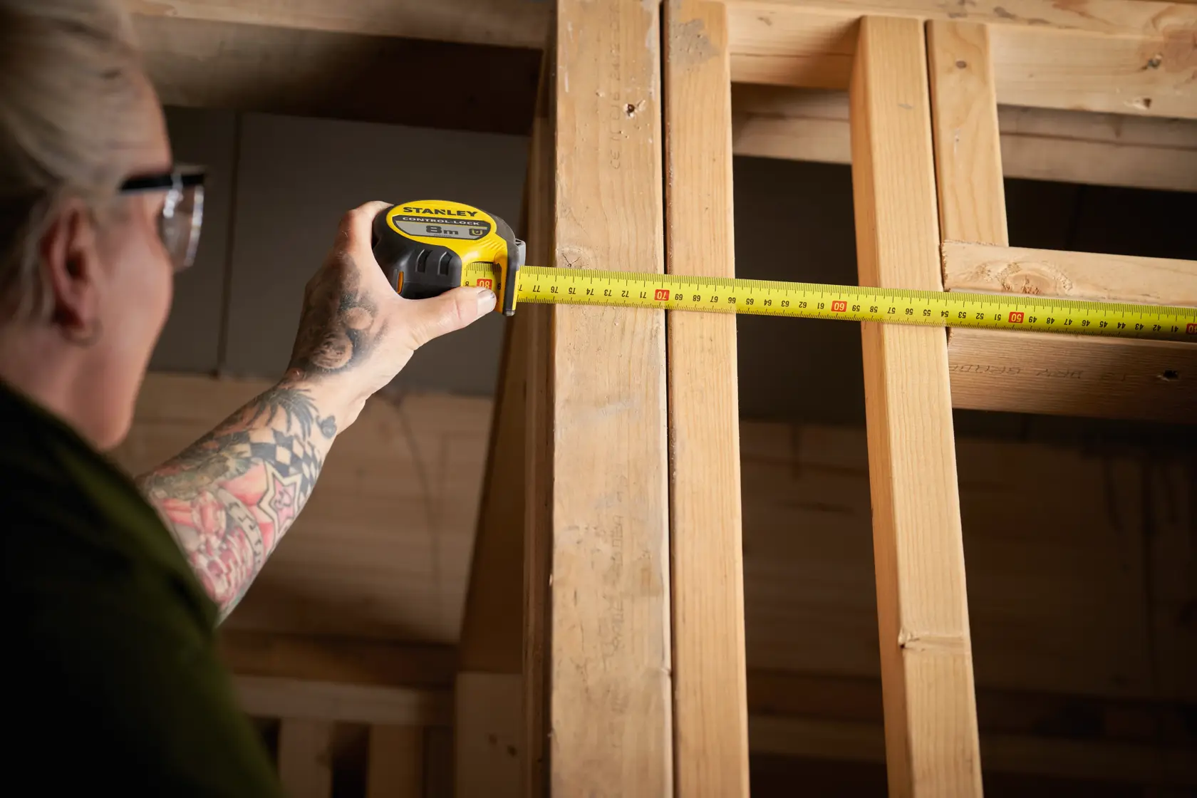 STANLEY STHT37232-0 metro a nastro in uso su travi di legno, utensile giallo e nero, angolo laterale.
