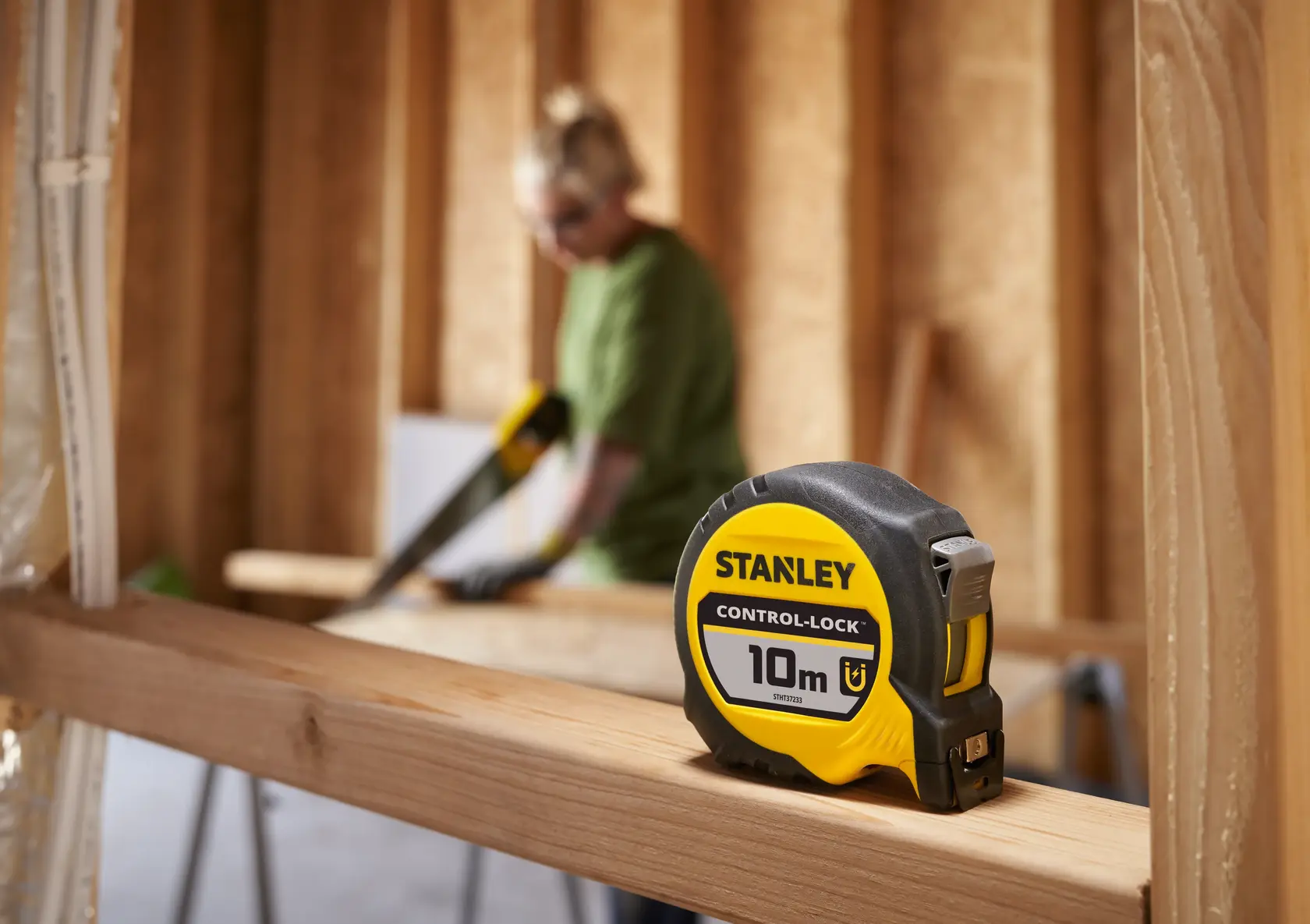 Stanley STHT37233-0 metro a nastro, 10 m, giallo e nero, su trave di legno con sfondo sfocato.