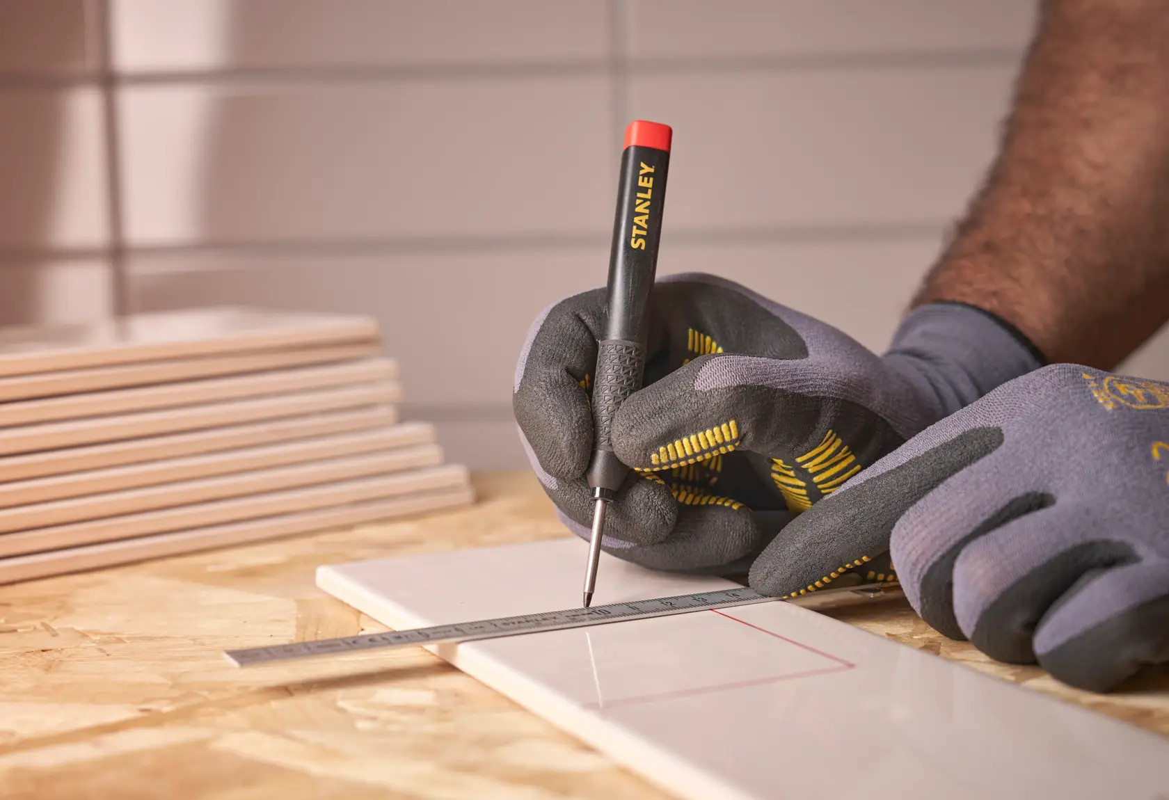 Mani guantate segnano una piastrella con utensile STANLEY e righello metallico.