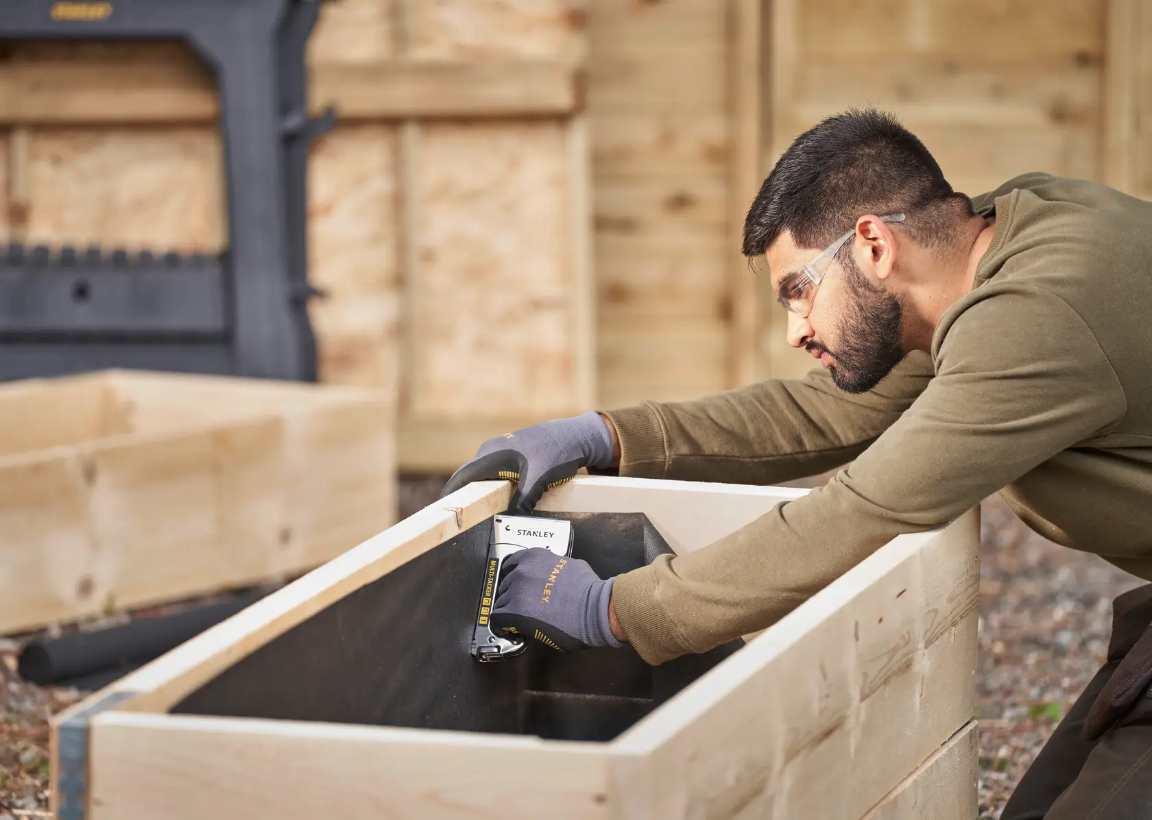 Foto della pinzatrice manuale STANLEY STHT6-70410 per lavori in legno, persona che fissa il rivestimento in una fioriera di legno all'aperto.