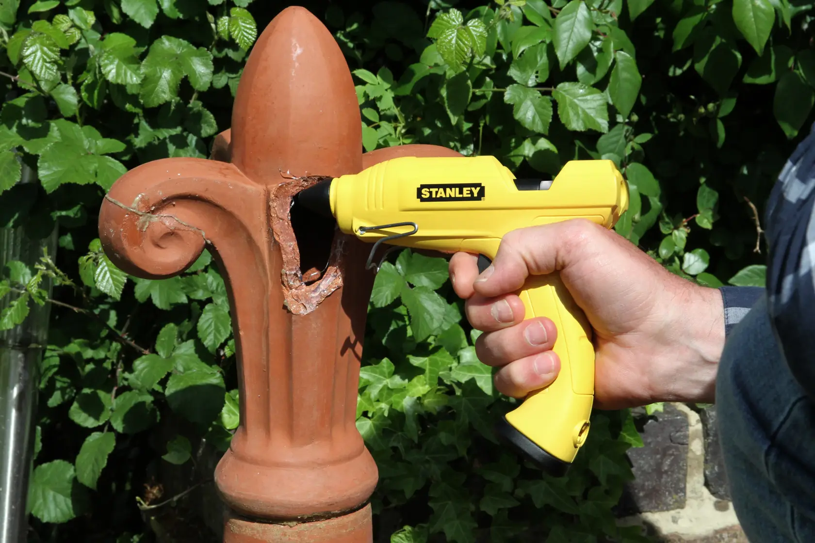 Stanley STHT6-70416 pistola colla gialla per riparare ornamento in terracotta all'aperto, tenuta in mano.