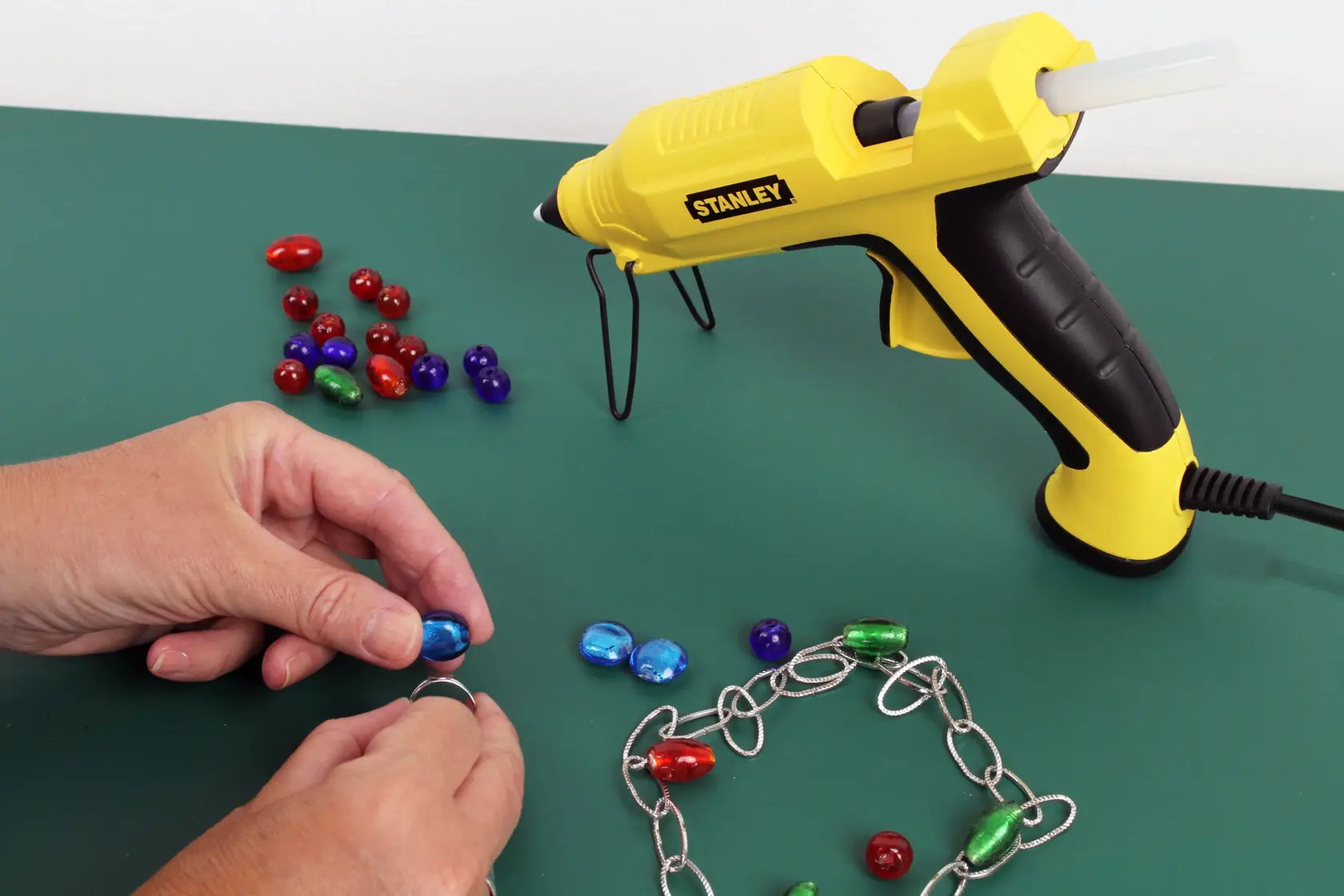 Stanley STHT6-70417 pistola per colla gialla per hobby con perline e catena su superficie verde.