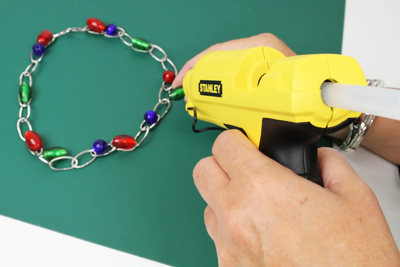 STANLEY STHT6-70417 pistola per colla gialla usata per assemblare una catena colorata di perle su superficie verde.