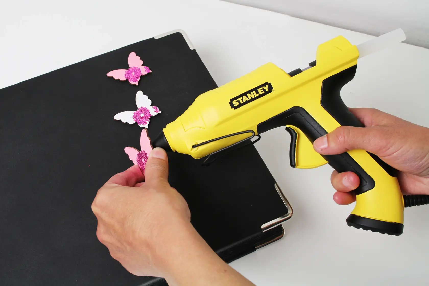 STANLEY STHT6-70417 pistola per colla gialla usata per decorare farfalle rosa su una cartella nera.
