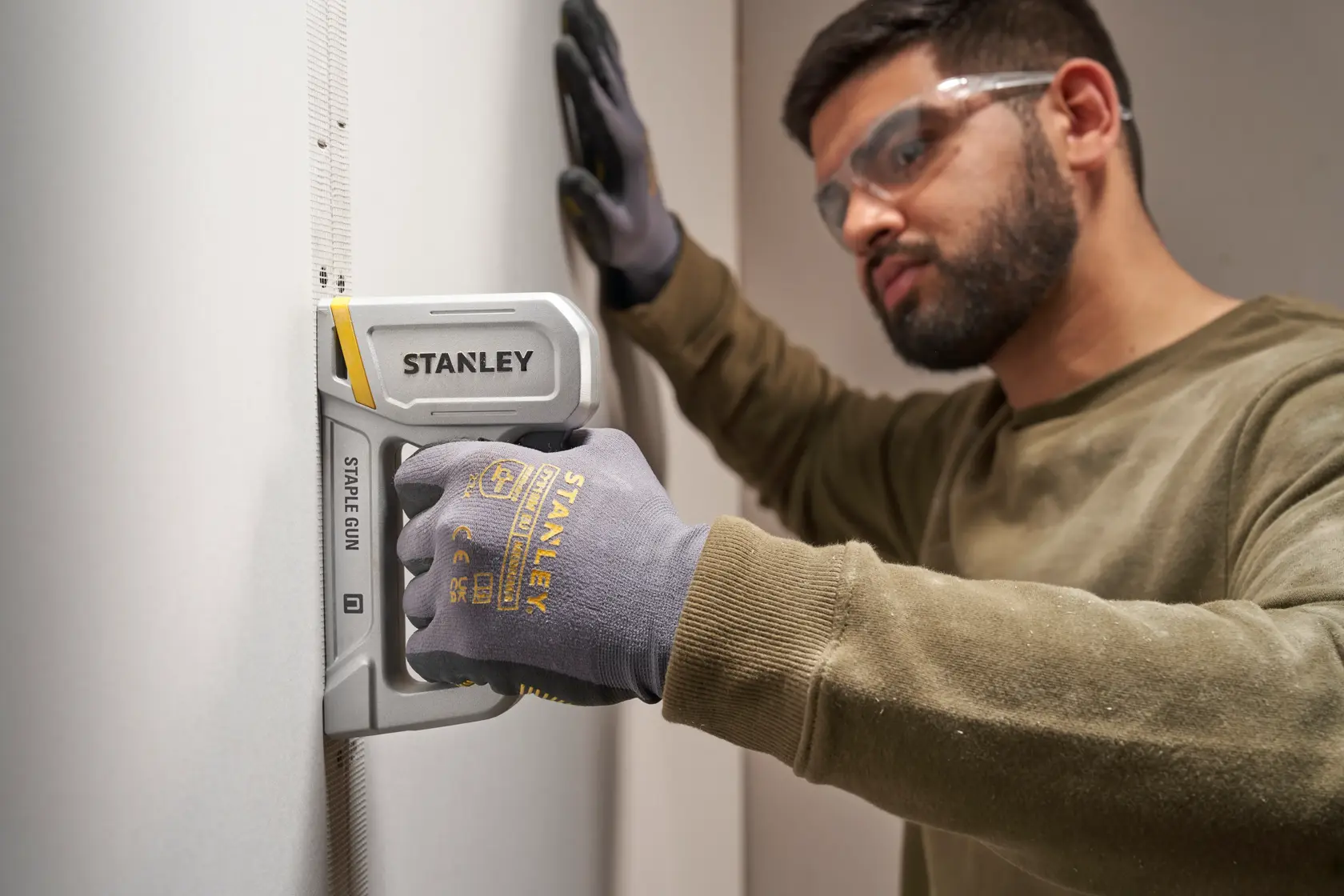 Fotografia della graffatrice STANLEY STHT70150-0 usata su una parete, persona con guanti STANLEY.