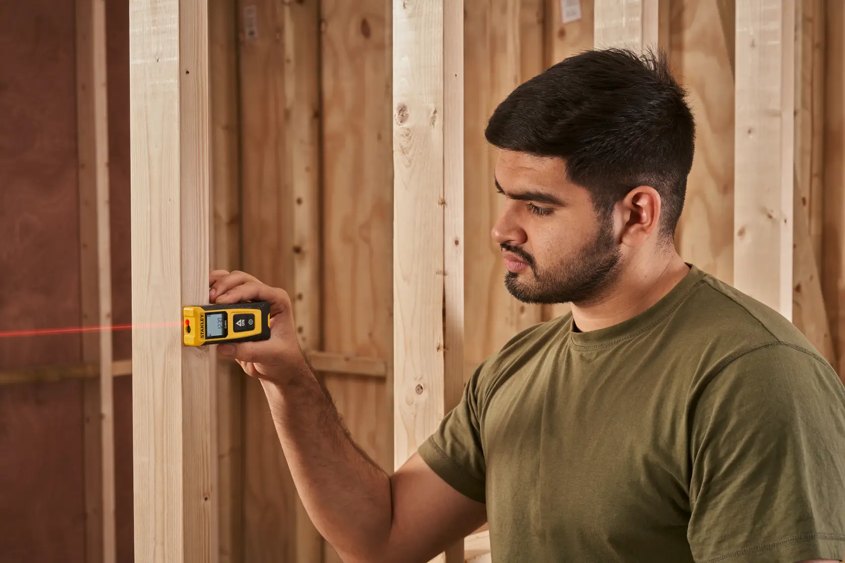 Foto del misuratore laser STANLEY STHT77065-0 in uso, misura montanti in legno in un cantiere.