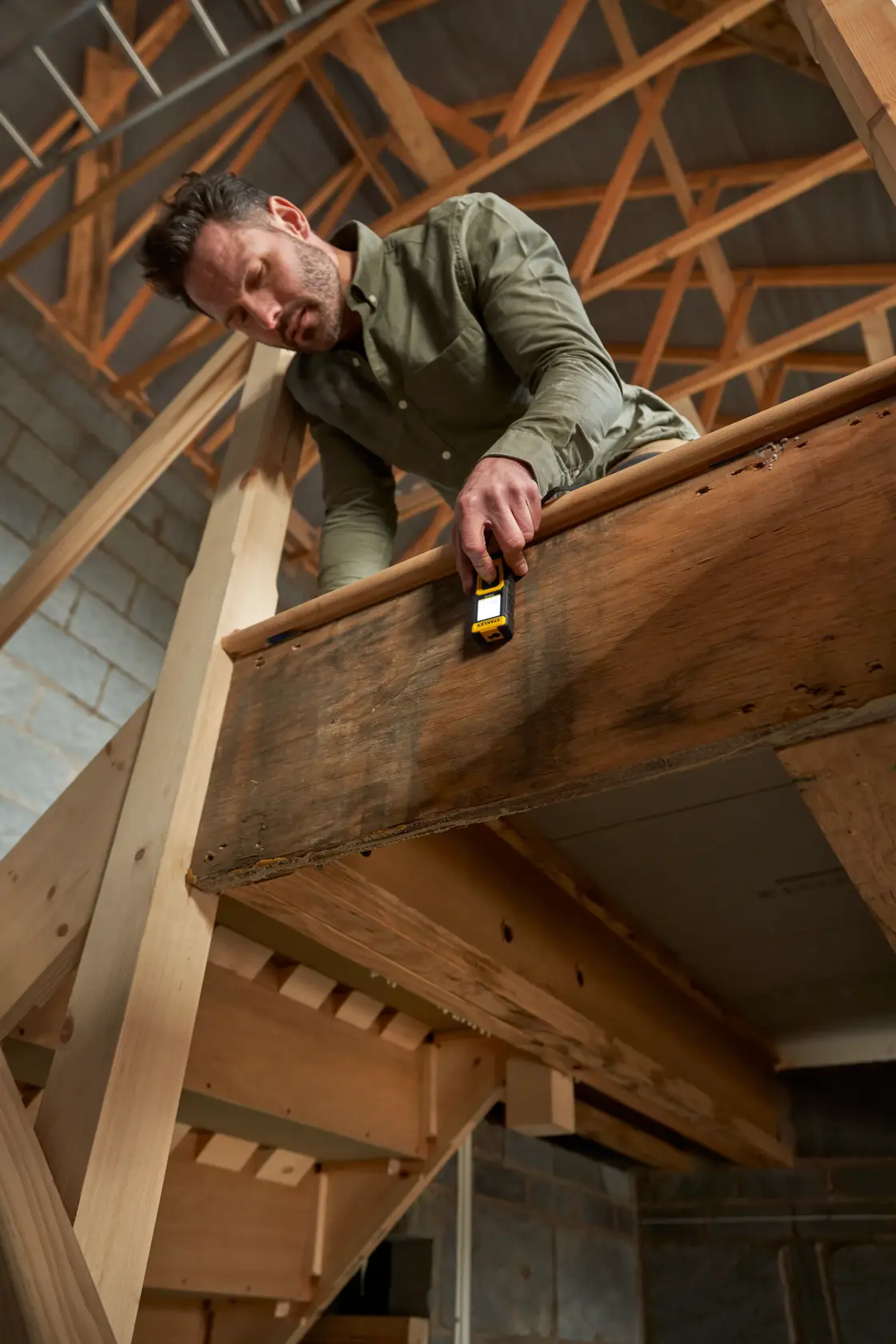 Foto del misuratore laser STANLEY STHT77100-0 in uso su una ringhiera di legno in un cantiere.