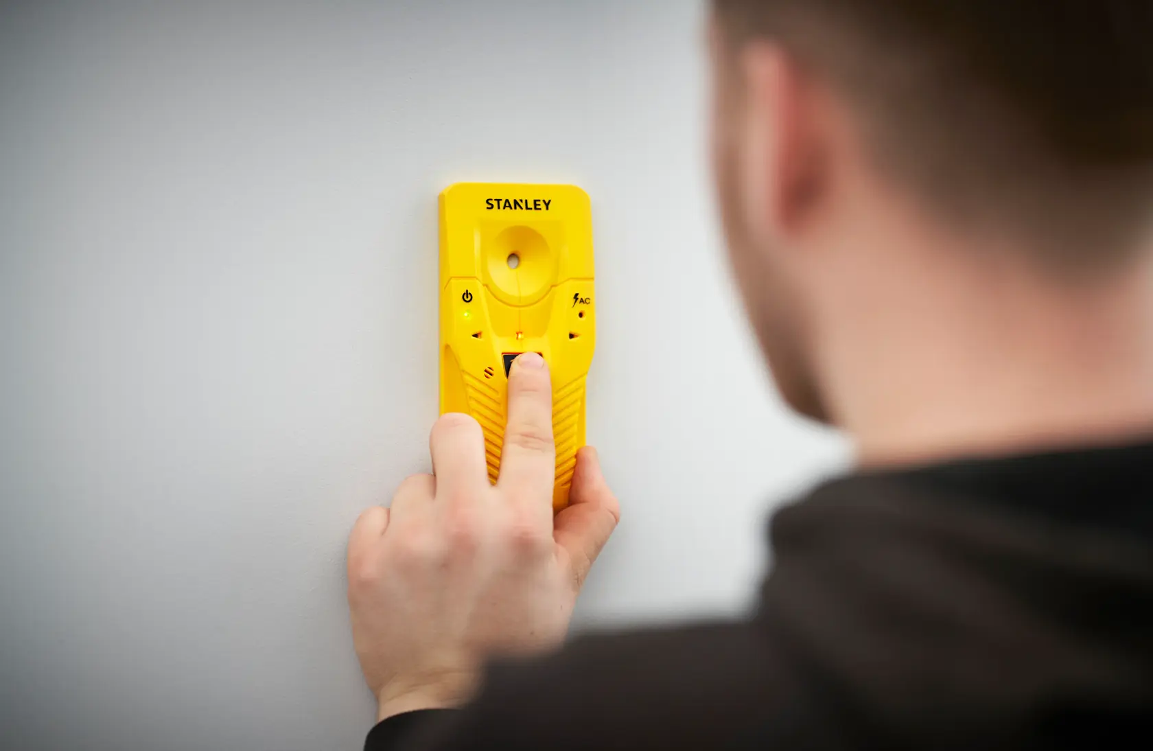 Foto di STANLEY STHT77587-0 rilevatore di travi giallo su una parete bianca, tenuto da una persona.