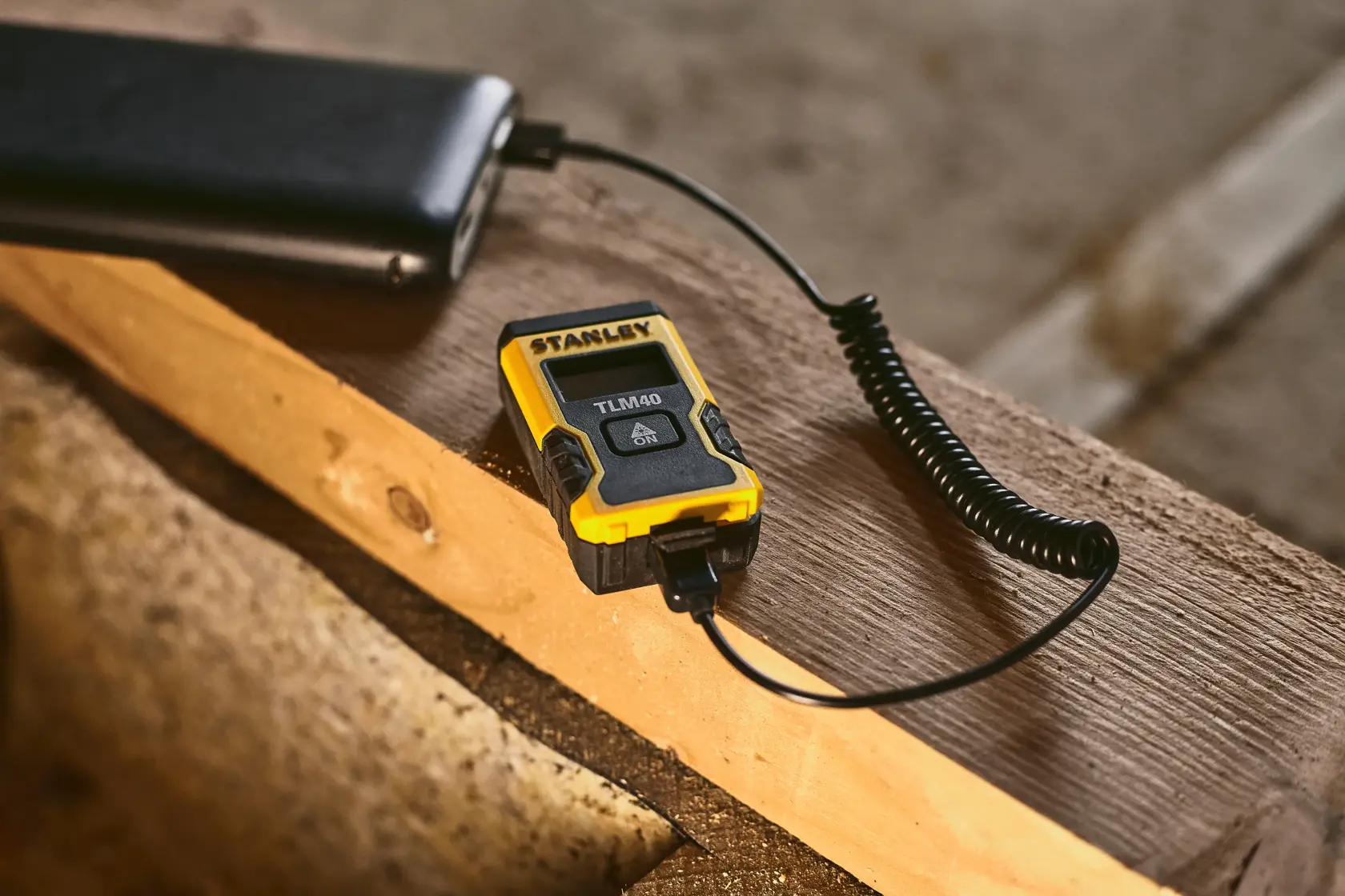 STANLEY STHT77666-0 misuratore laser di distanza in ricarica con cavo USB su superficie di legno.