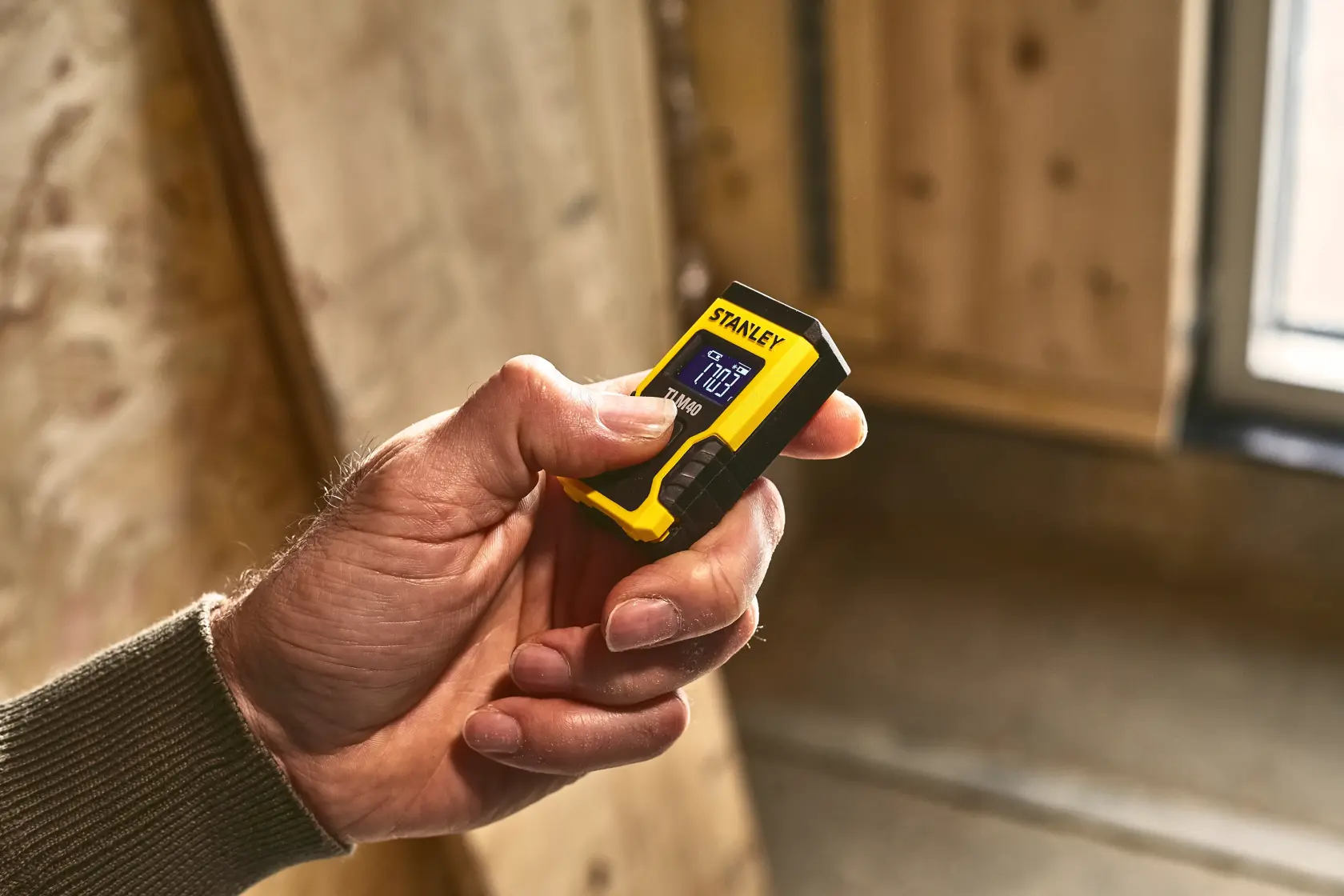 Misuratore laser compatto STANLEY STHT77666-0 giallo e nero tenuto in mano, ambiente interno.