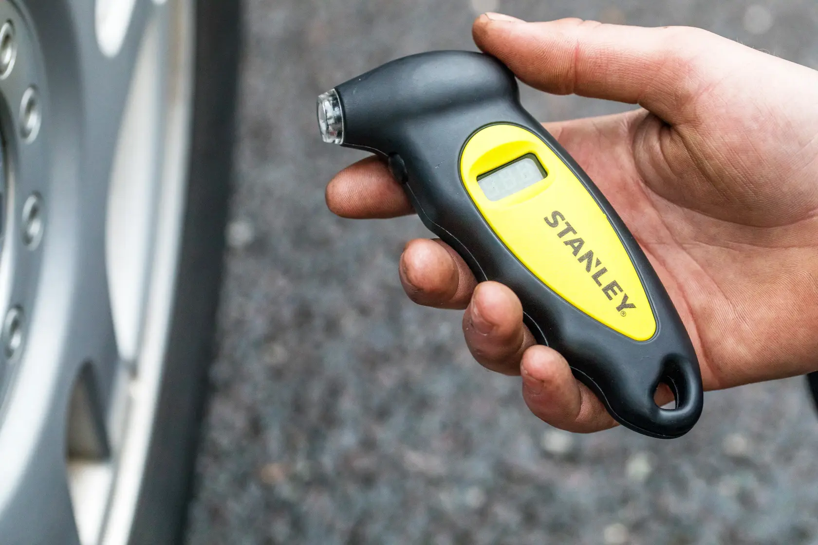 Stanley STHT80874-0 misuratore digitale pressione pneumatici tenuto in mano vicino alla ruota, nero e giallo.
