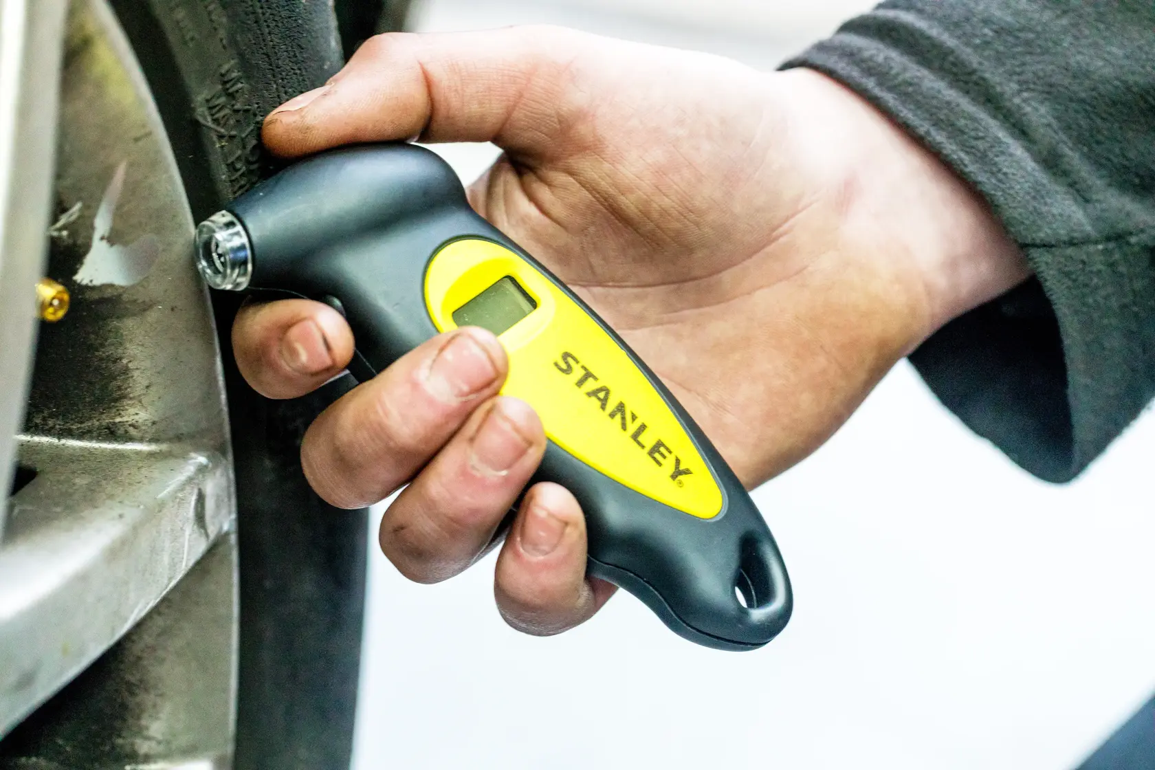 STANLEY STHT80874-0 misuratore pressione pneumatici tenuto vicino a una ruota dell’auto.