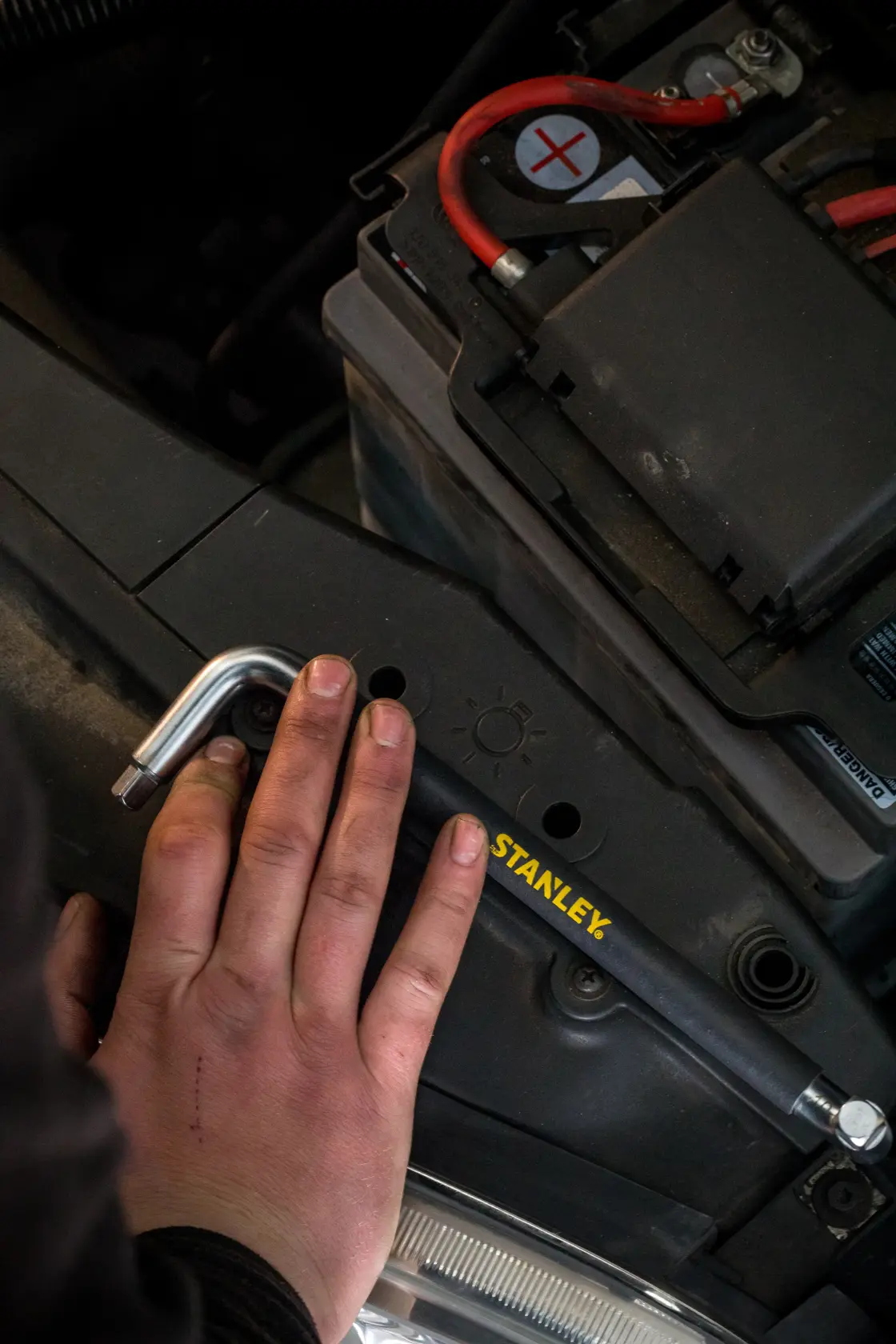 Foto della chiave esagonale STANLEY STHT80879-0 in uso su una batteria auto, vista ravvicinata con mano.