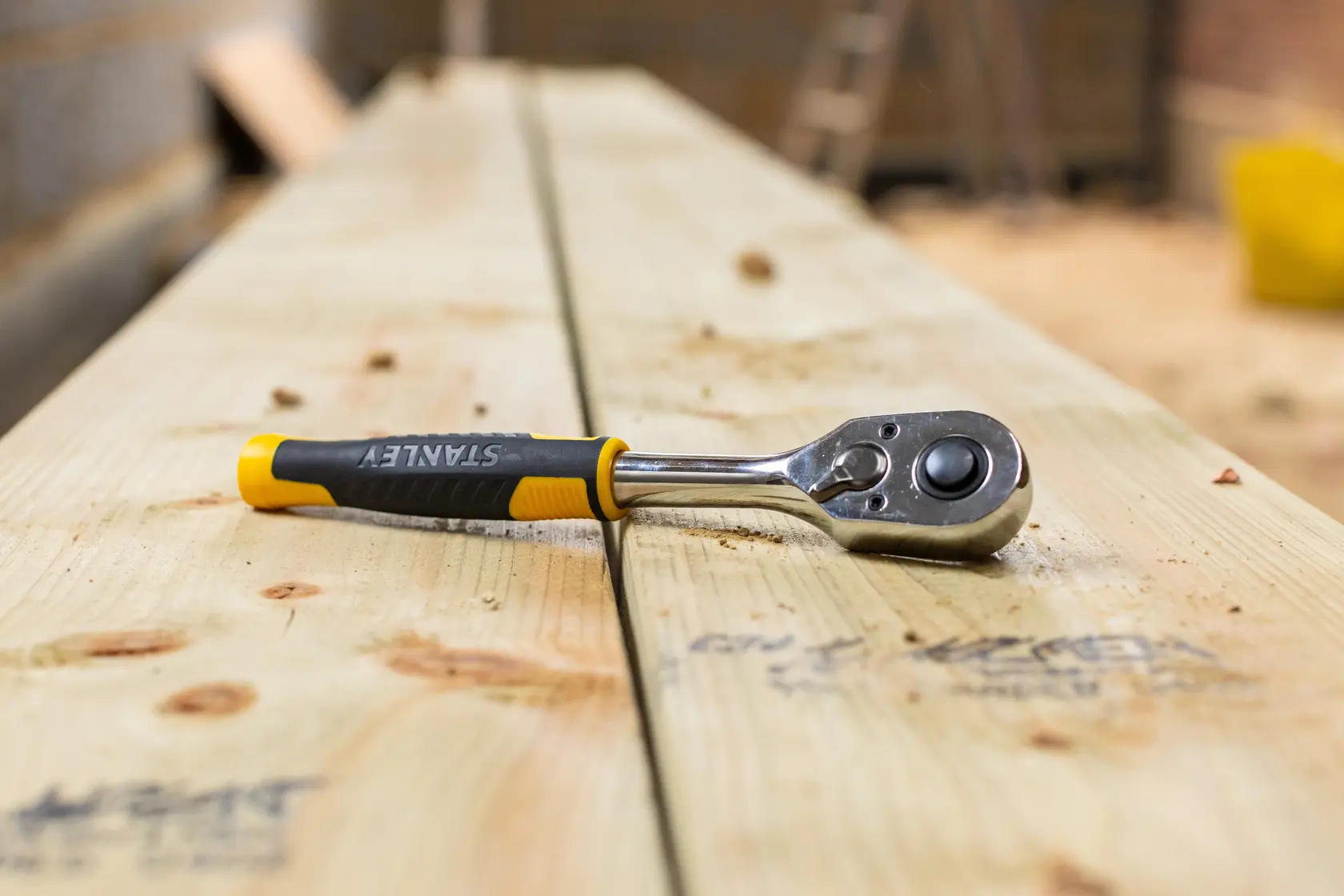 Cricchetto STANLEY STMT82664-0 con manico nero e giallo su assi di legno, vista laterale.