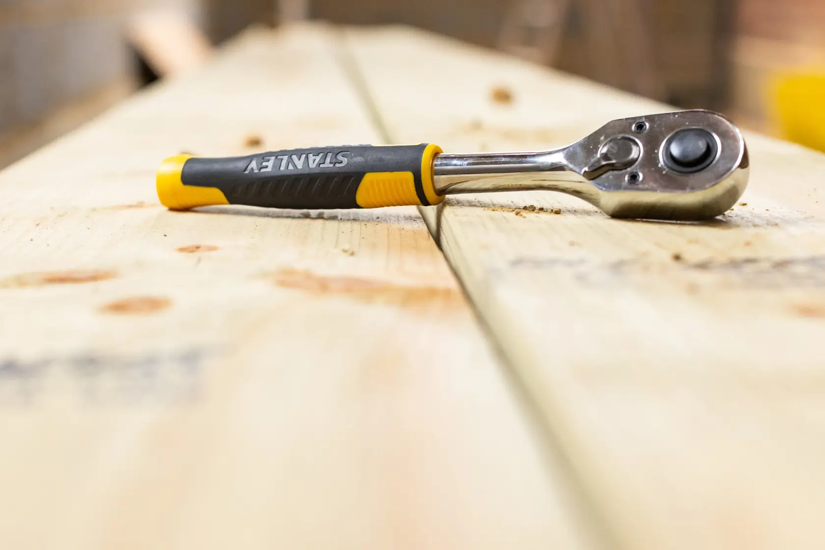 Chiave a cricchetto STANLEY STMT82664-0 con manico nero e giallo su assi di legno, fotografia ravvicinata.