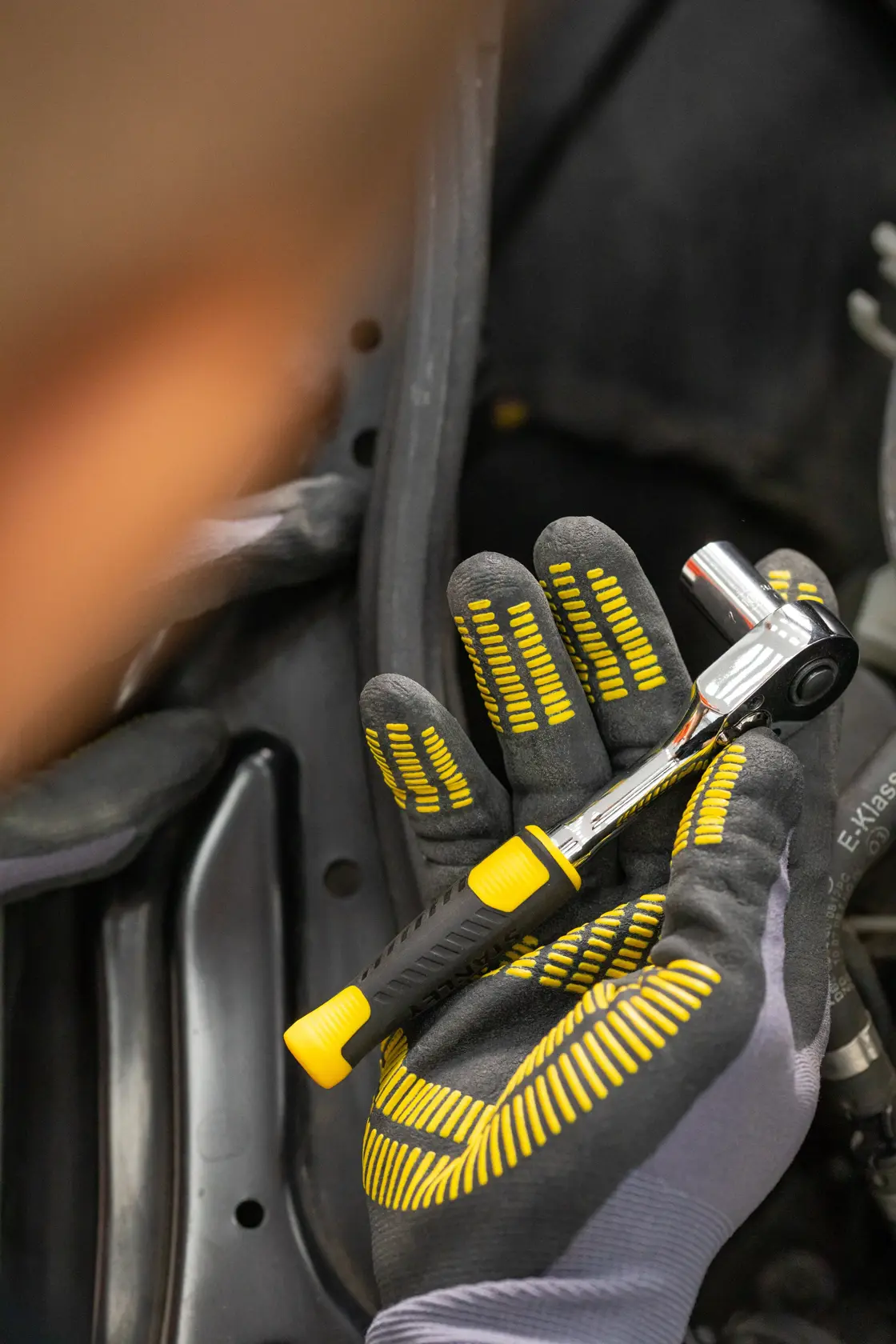 Chiave a cricchetto STANLEY STMT82828-1 con manico nero e giallo, tenuta in mano con guanto, primo piano.