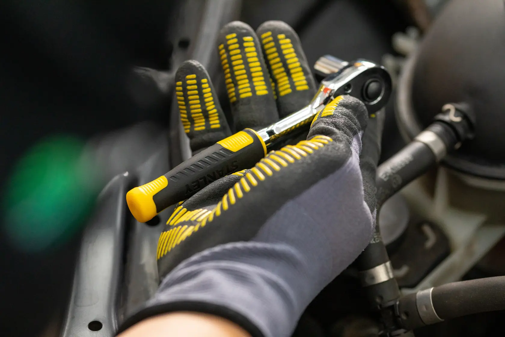 STANLEY STMT82831-1 chiave a cricchetto tenuta da mano con guanto, manico nero e giallo, contesto automobilistico.