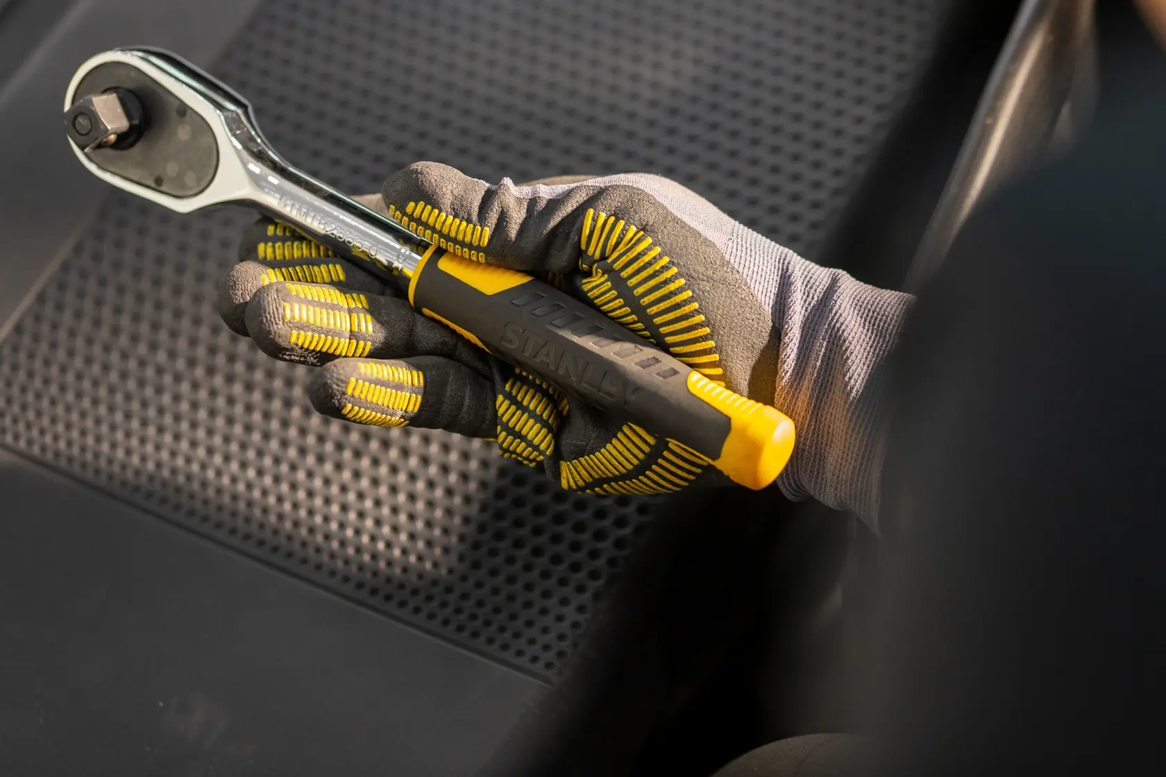 Chiave a cricchetto STANLEY STMT82832-1 con manico giallo tenuta da mano guantata su sedile nero.