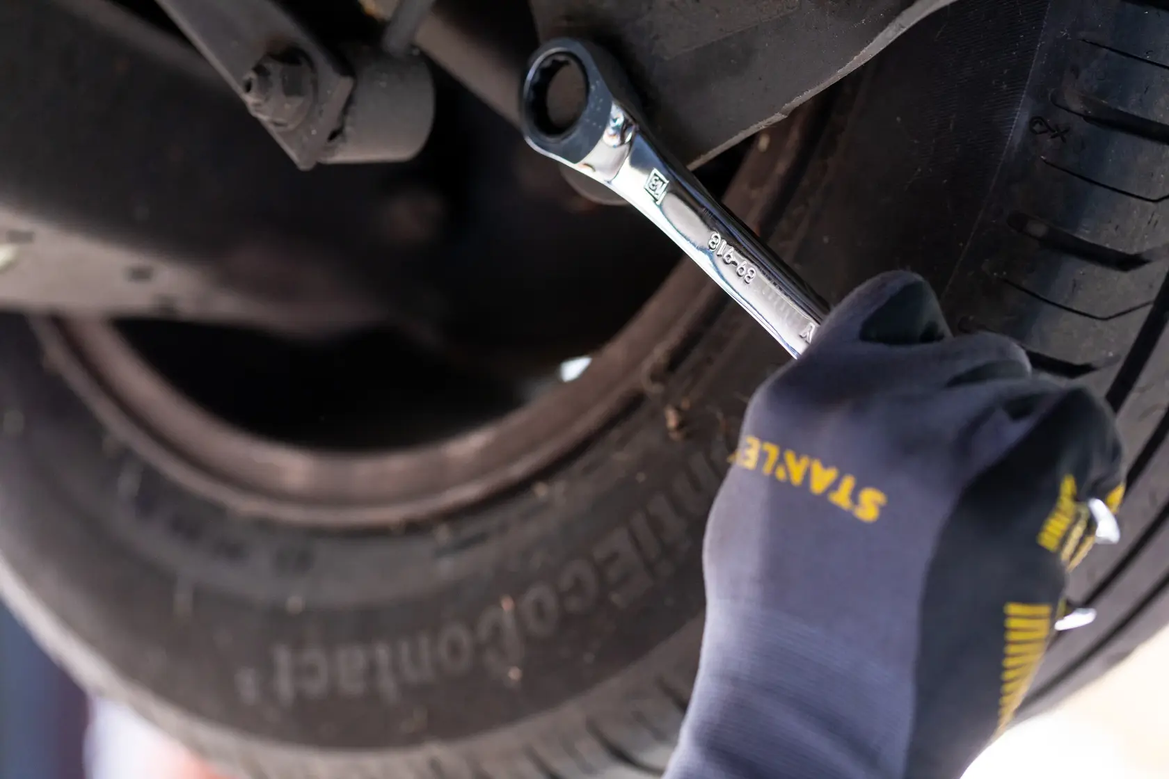 Chiave STANLEY STMT82847-0 usata sulla ruota dell’auto da mano con guanto in contesto automobilistico ravvicinato.