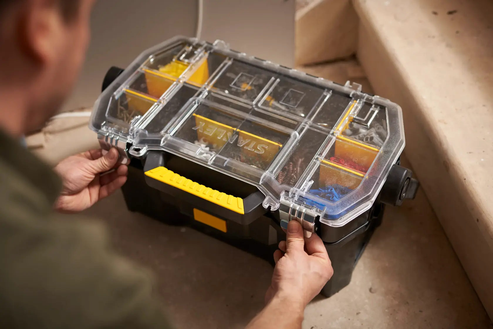 Organizer per attrezzi STANLEY STST1-70317 con coperchio trasparente e manico giallo, aperto sul cantiere.