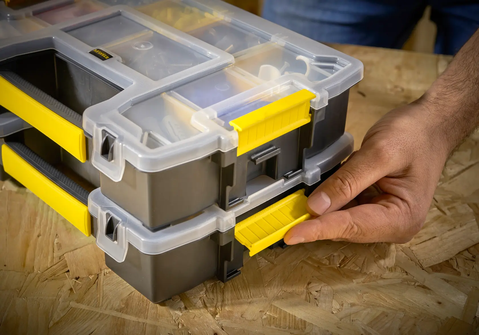 STANLEY STST1-70720 scatola organizer con chiusura gialla, impilata, primo piano di mano che apre la chiusura.