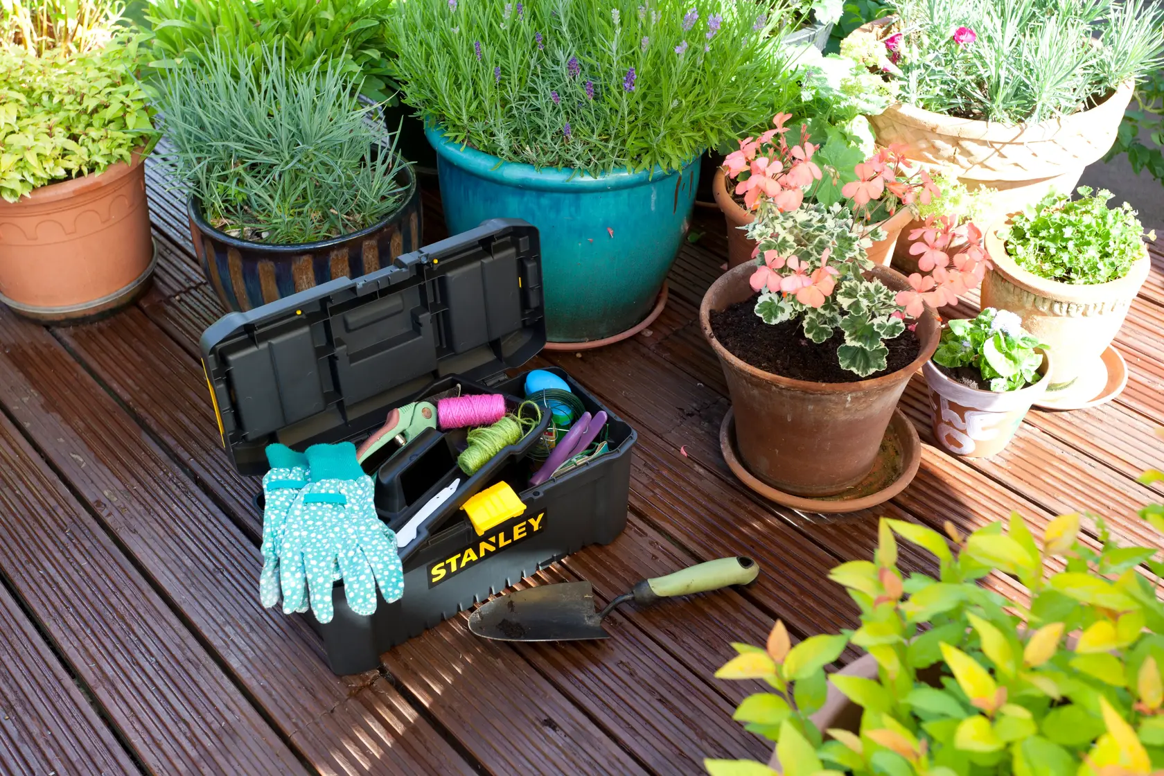 Stanley STST1-75517 cassetta degli attrezzi con attrezzi da giardinaggio e guanti su terrazza in legno vicino a vasi, angolo esterno.
