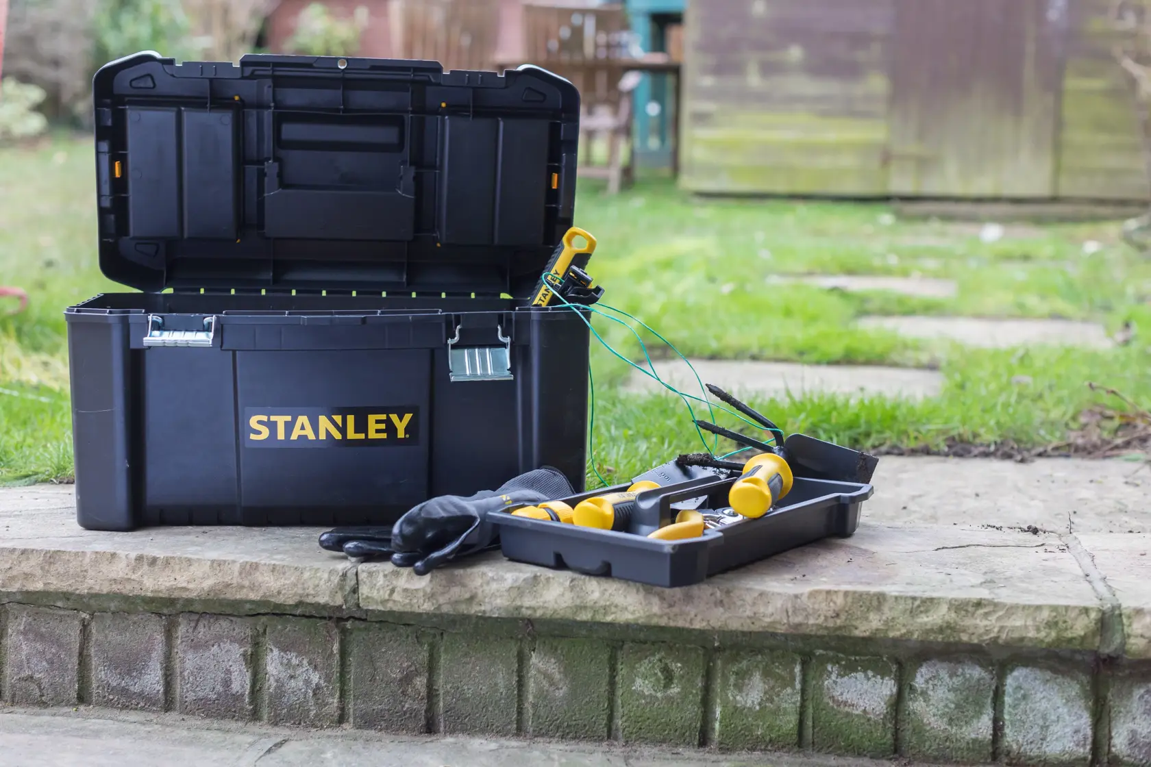 STANLEY STST1-75521 cassetta degli attrezzi nera aperta con strumenti gialli e guanti su un gradino di pietra.