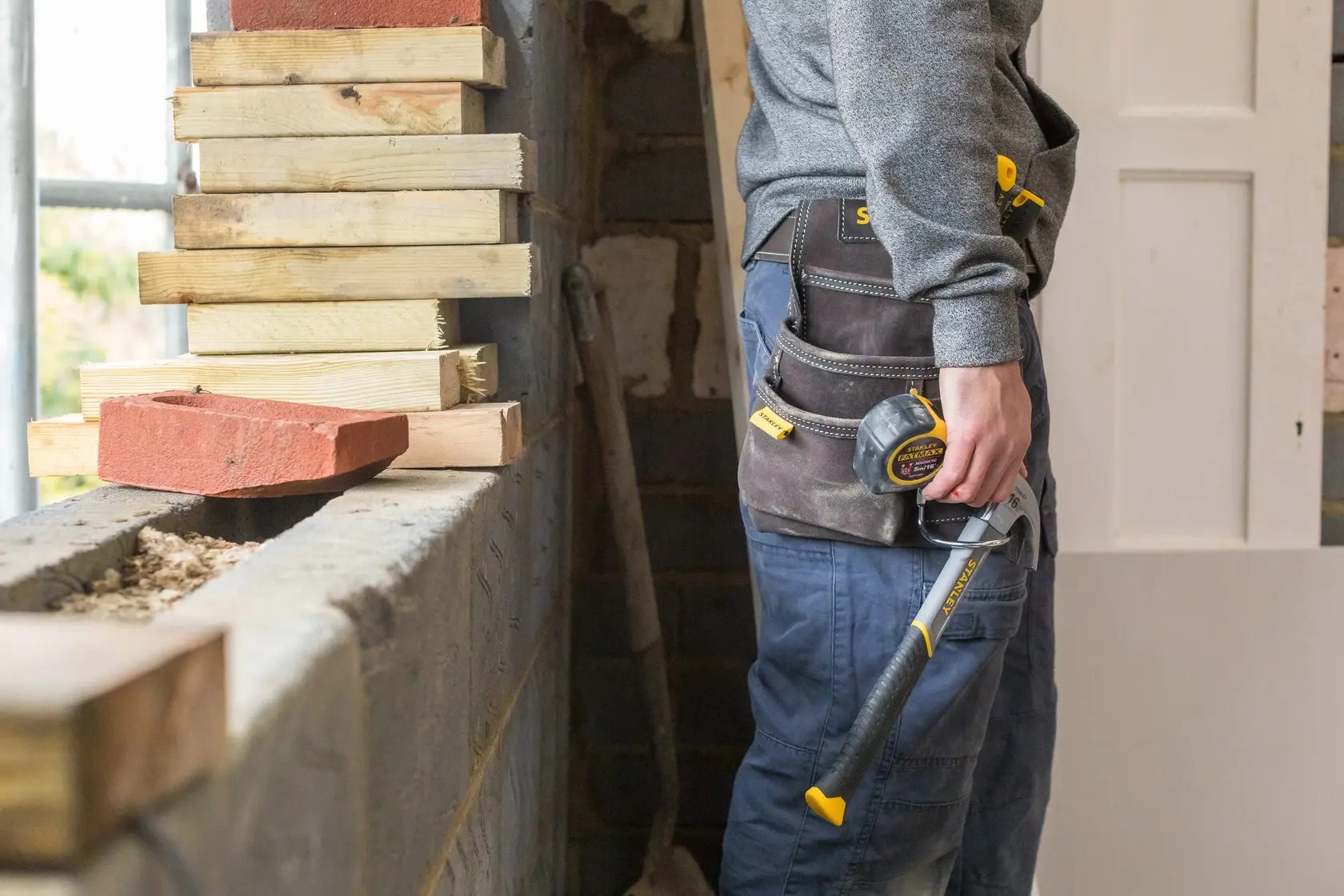 STANLEY STST1-80114 cintura porta attrezzi indossata da operaio con martello e metro, ambiente cantiere