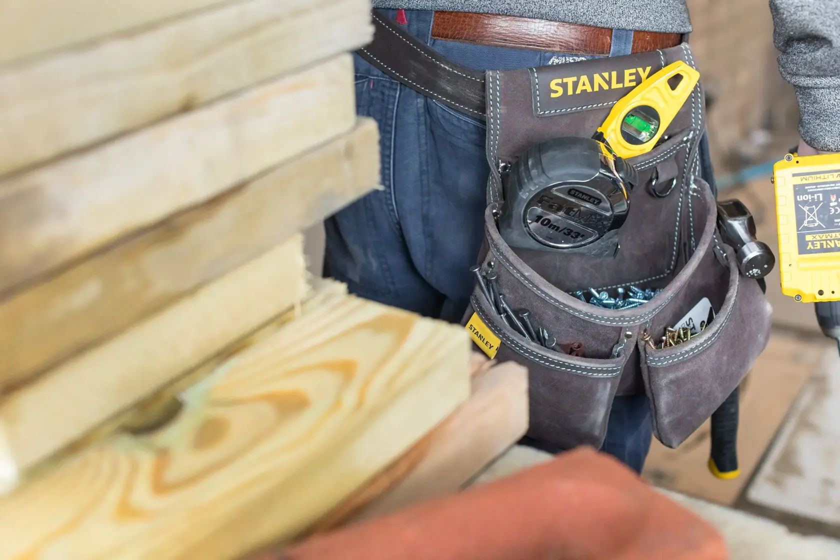 Foto della cintura porta attrezzi STANLEY STST1-80116 con utensili e componenti, indossata vicino a tavole di legno.