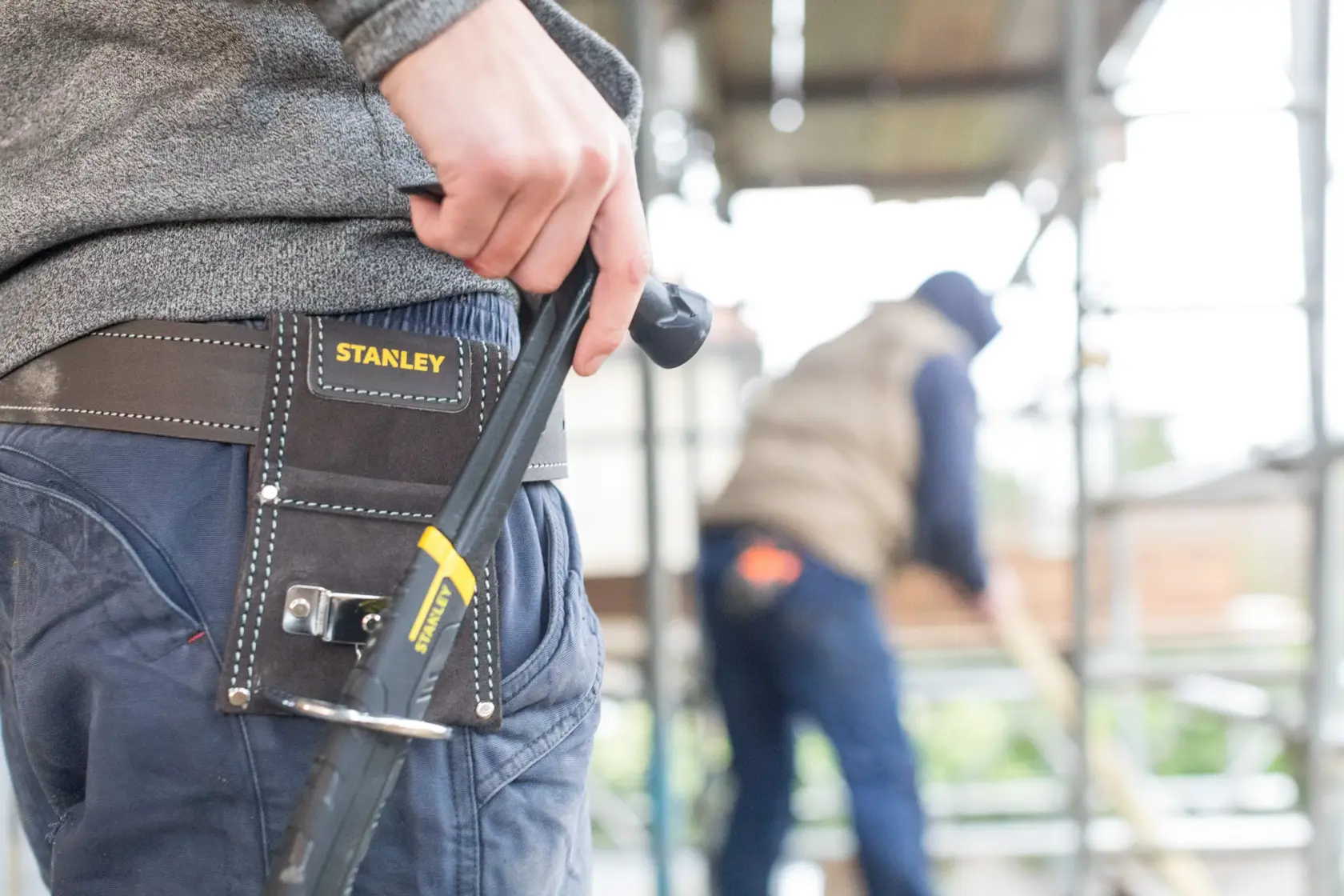 Cintura portautensili STANLEY STST1-80117 alla vita del lavoratore con utensile STANLEY, sfondo cantiere.