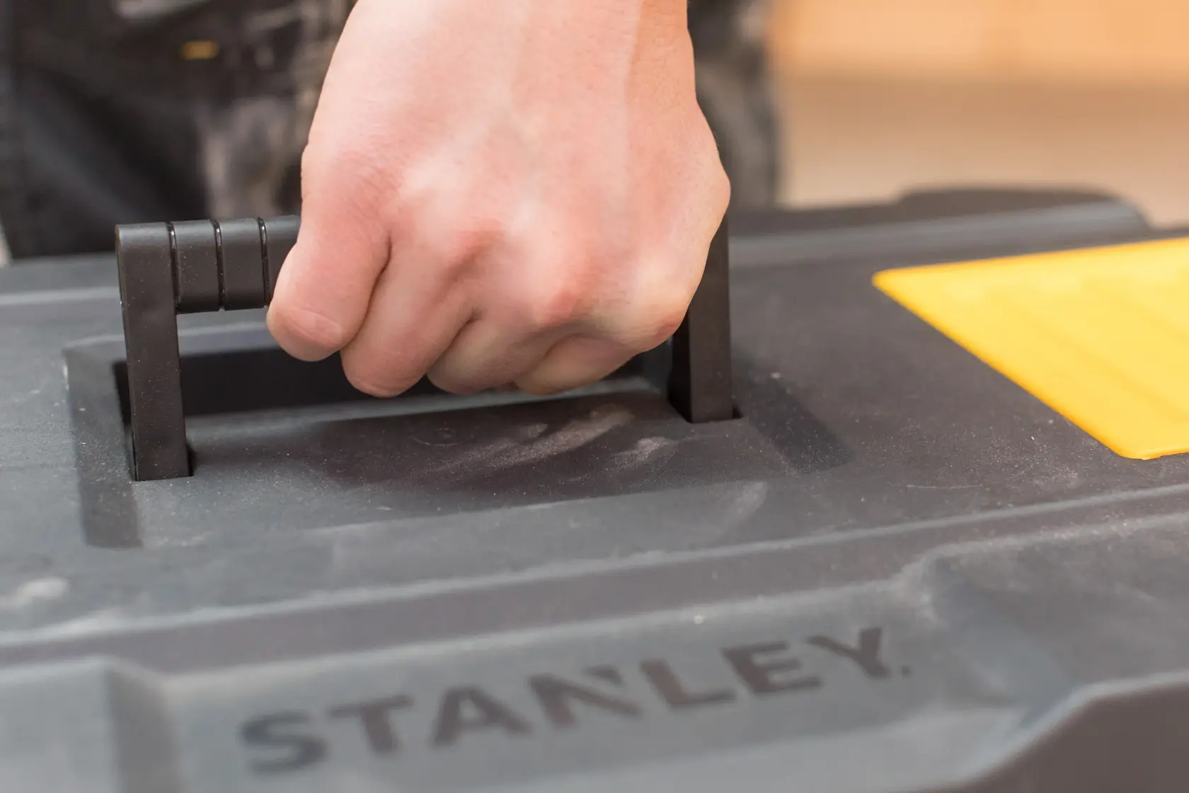 STANLEY STST1-80150 cassetta degli attrezzi primo piano, mano sulla maniglia nera, dettaglio giallo visibile.