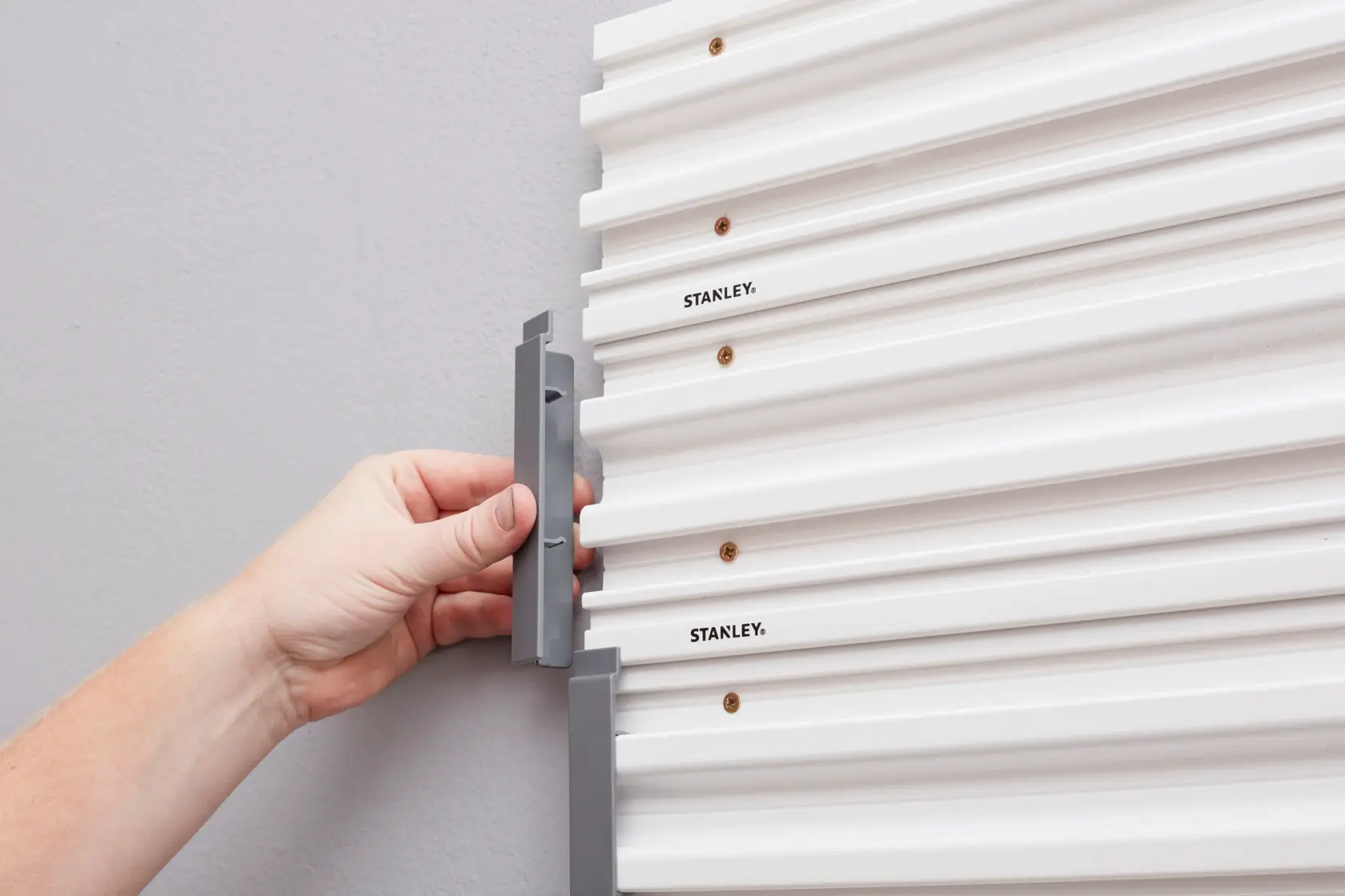 STANLEY STST82611-1 mano installa gancio grigio su pannello da parete bianco, vista laterale ravvicinata.