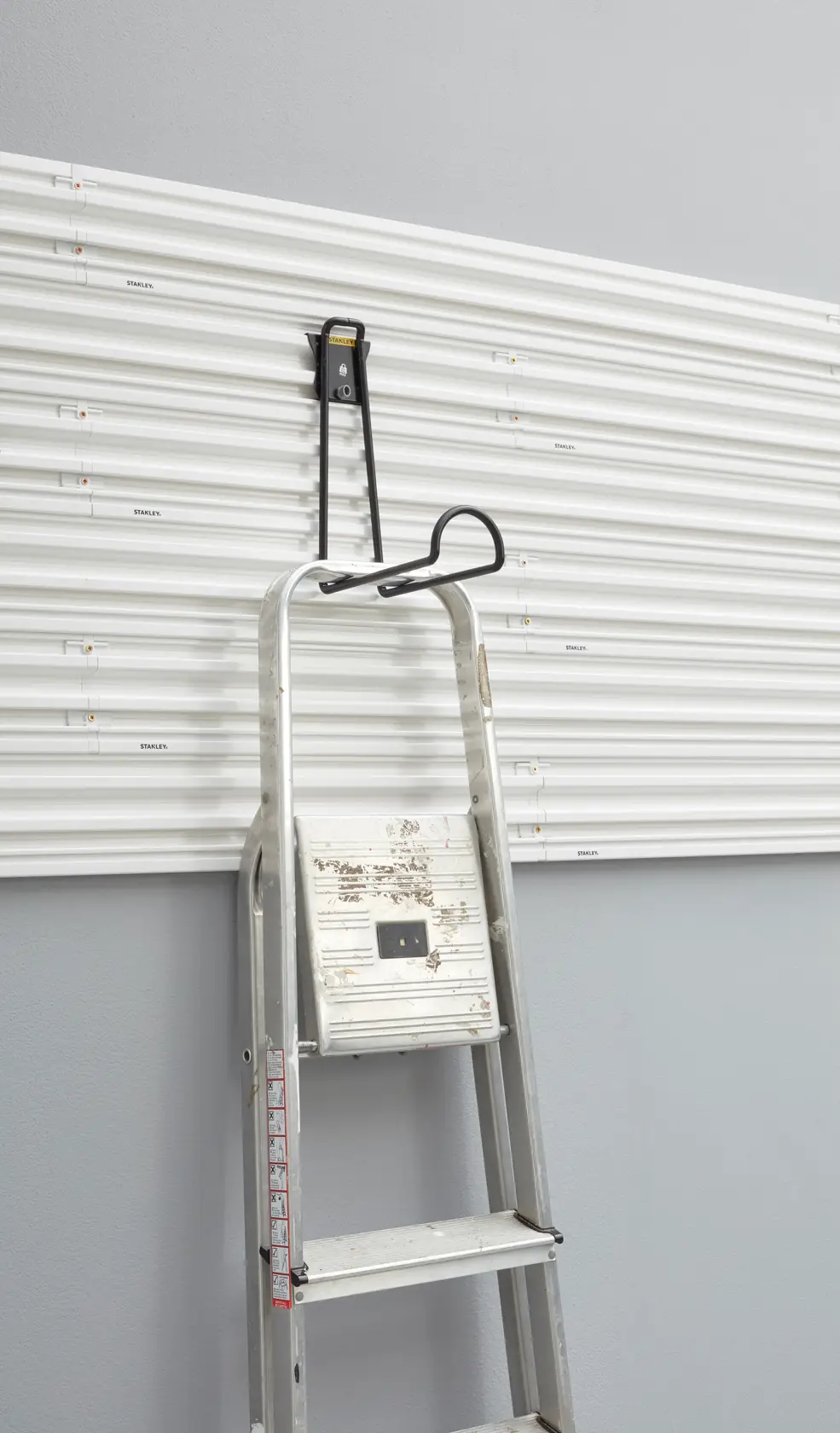 Gancio per scala STANLEY STST82614-1 su pannello da parete bianco, vista frontale.