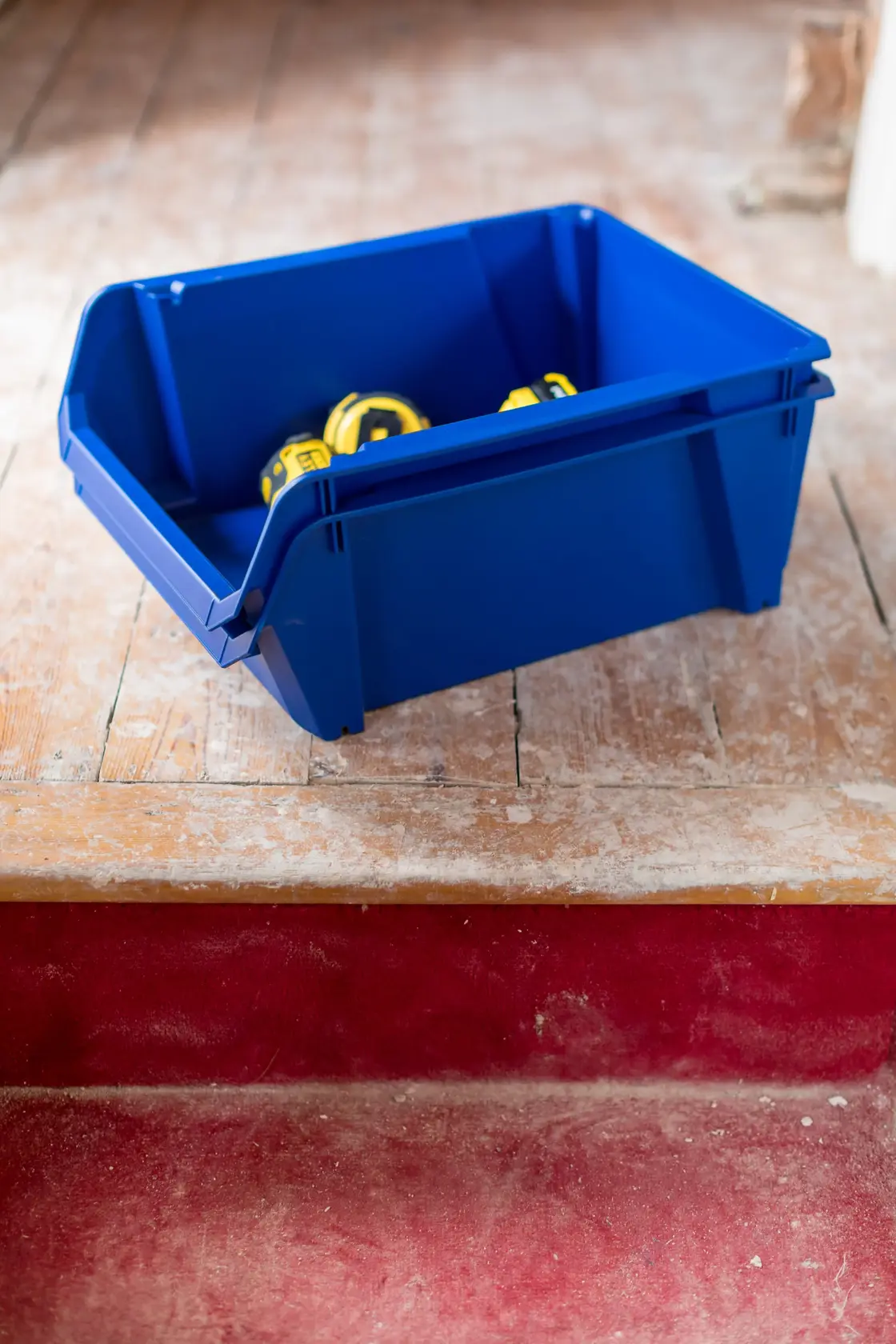 STANLEY STST82746-1 contenitore blu con metri a nastro gialli, in posizione angolata su pavimento in legno.